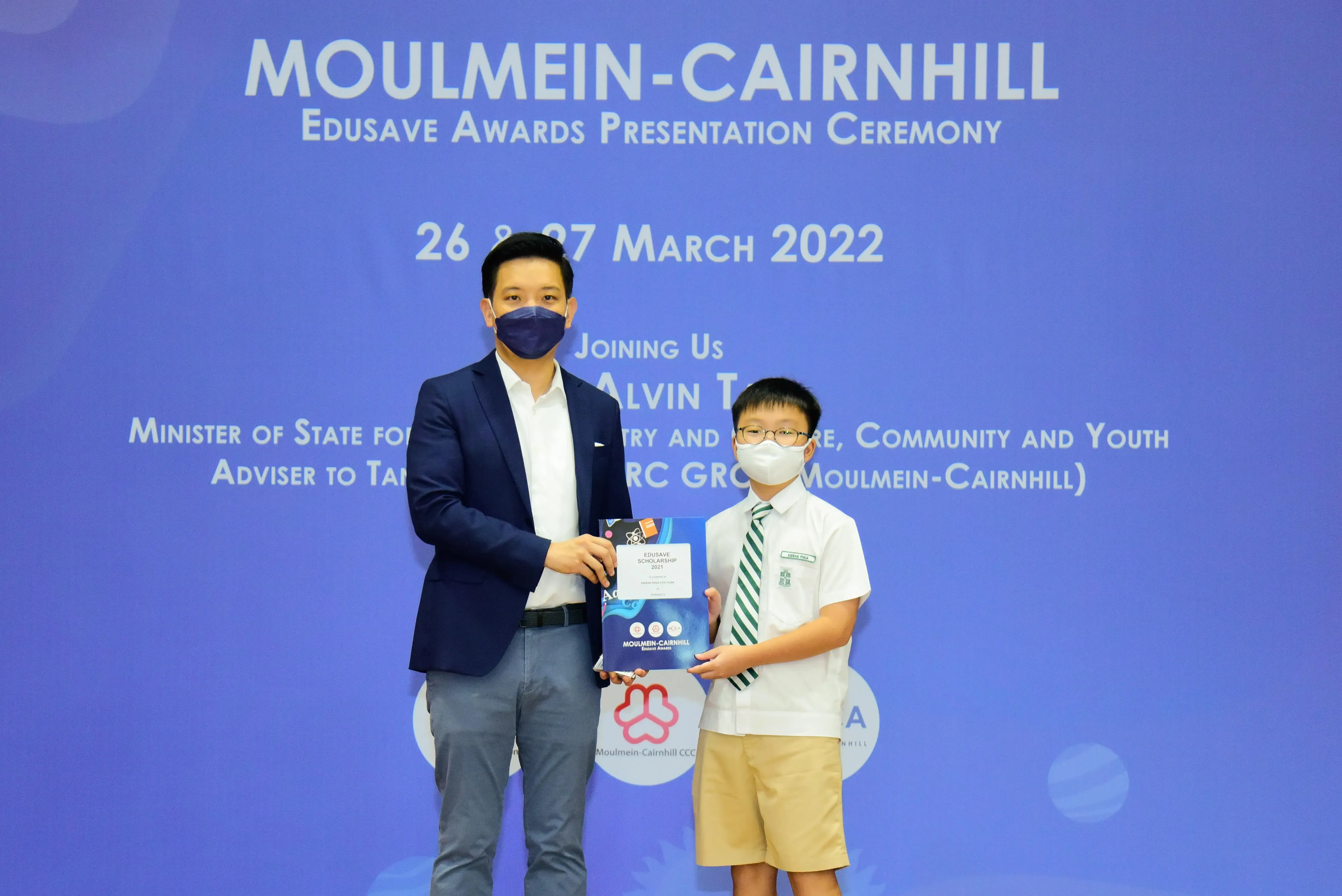 An adult and a young student in uniform hold an award certificate at the Moulmein-Cairnhill Edusave Awards Ceremony 2022.