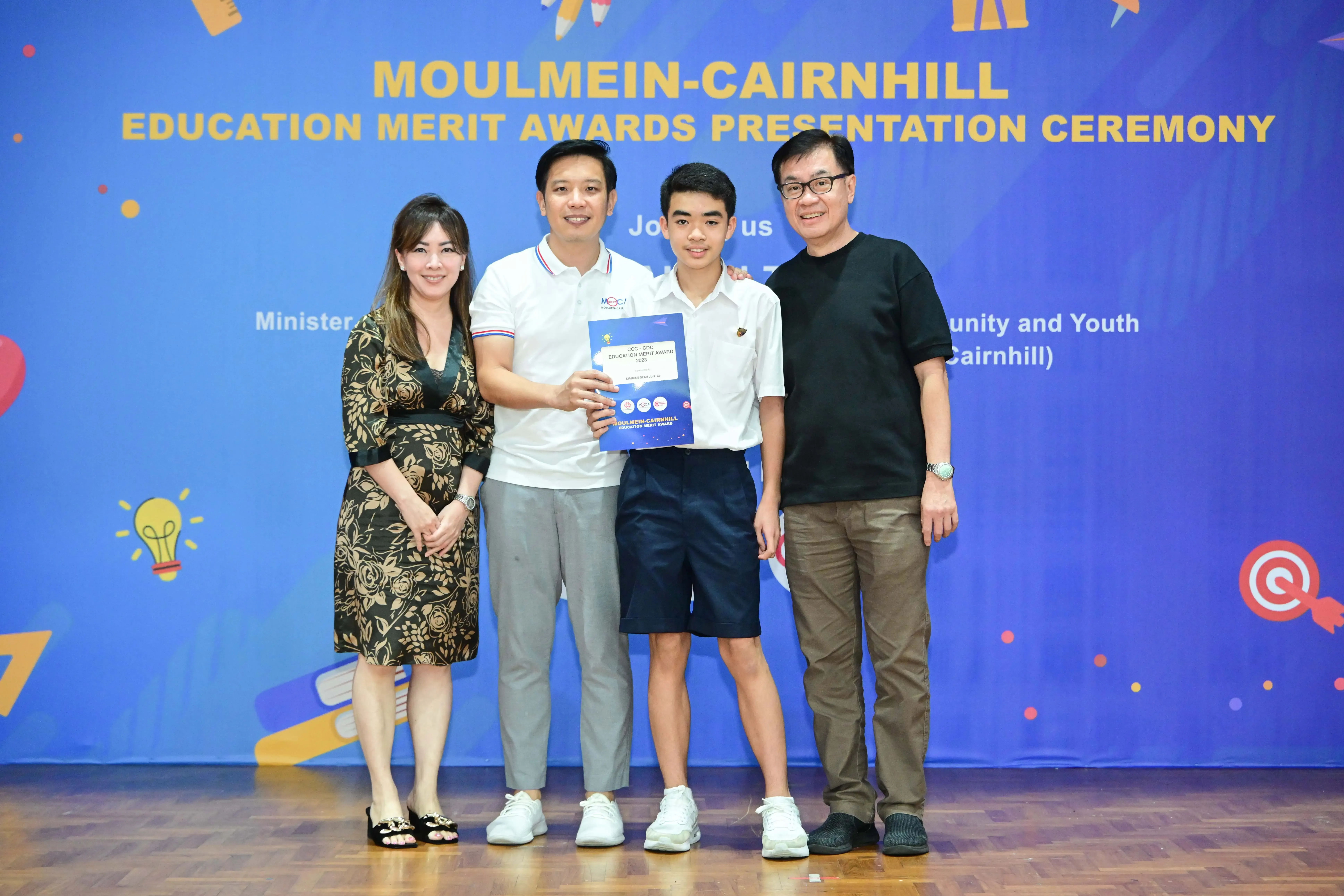 Four people posing at the Moulmein-Cairnhill Education Merit Awards Presentation Ceremony, with a student holding a certificate.