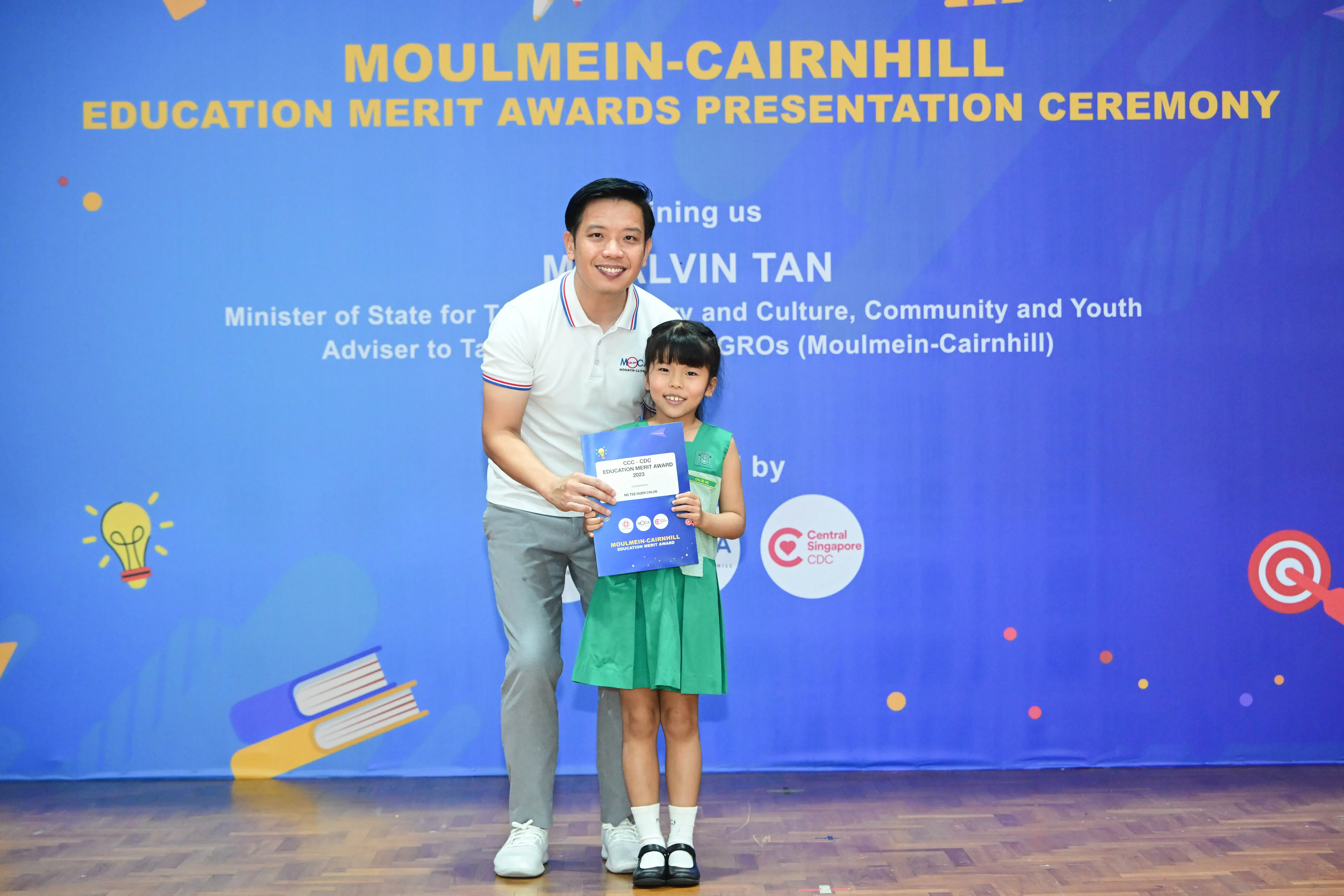 A man and a young girl holding a certificate at the Moulmein-Cairnhill Education Merit Awards Presentation Ceremony.