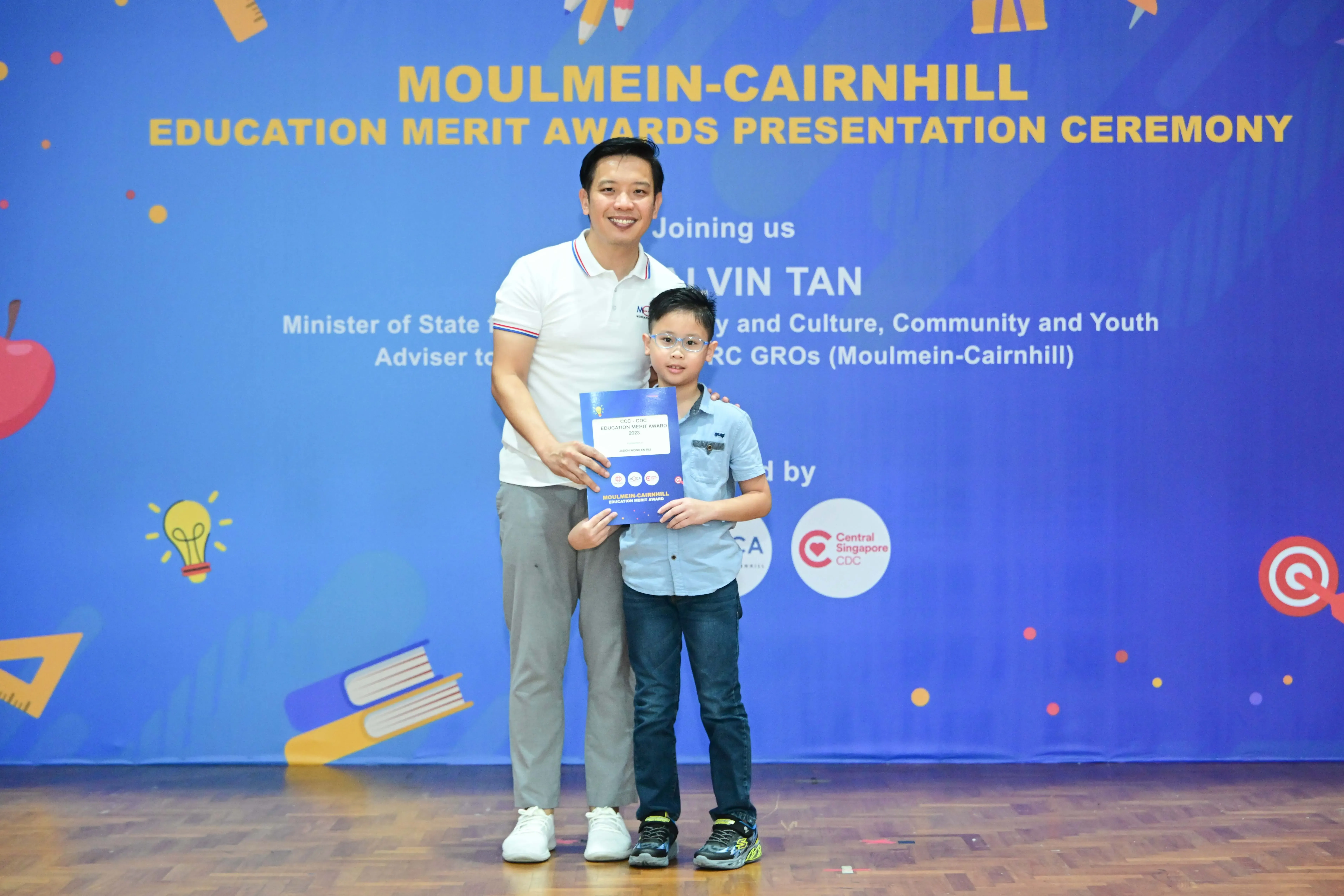 A man and a young boy pose together holding a certificate at the Moulmein-Cairnhill Education Merit Awards ceremony.