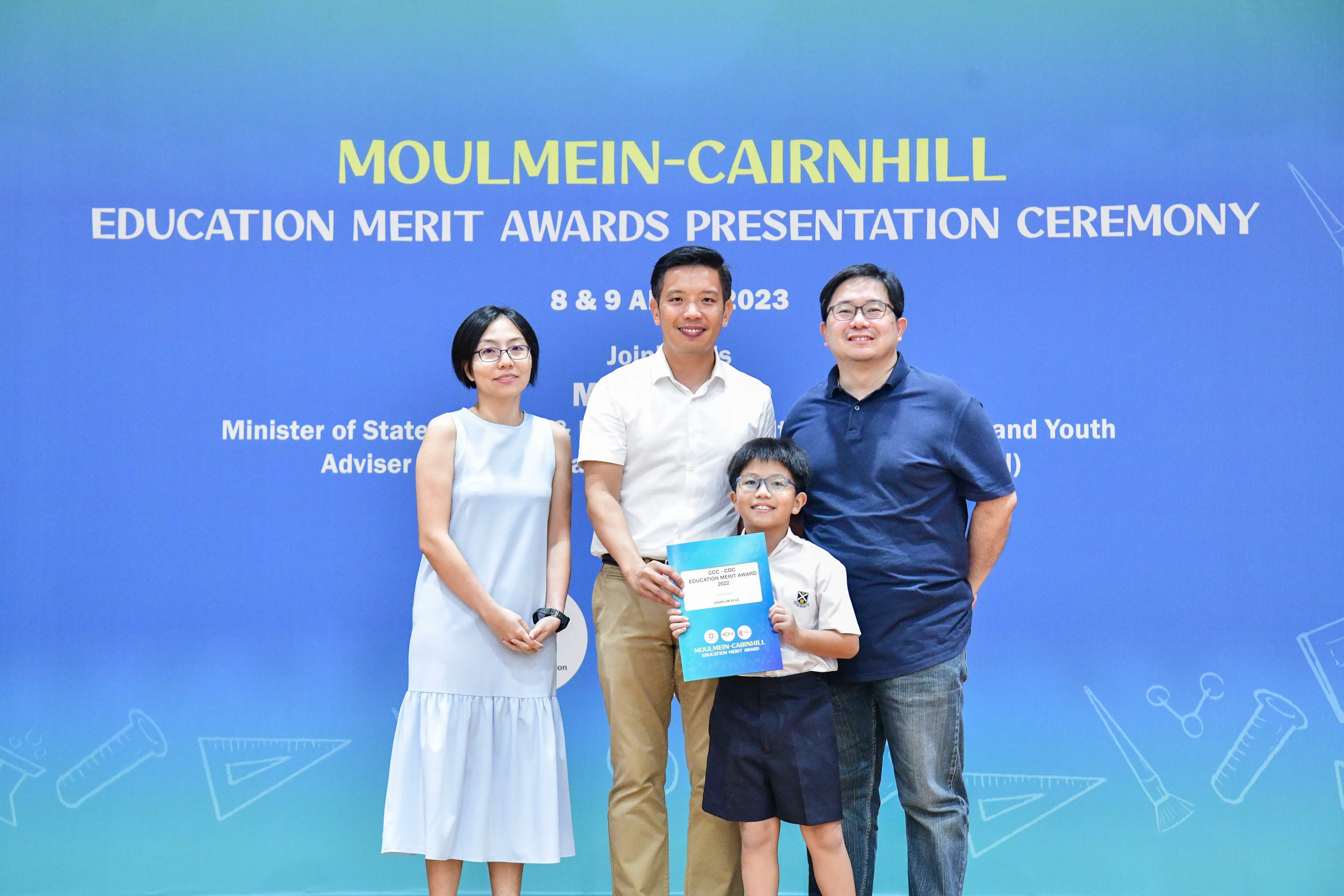 Three adults and a boy holding a certificate pose at the Moulmein-Cairnhill Education Merit Awards Ceremony 2023.