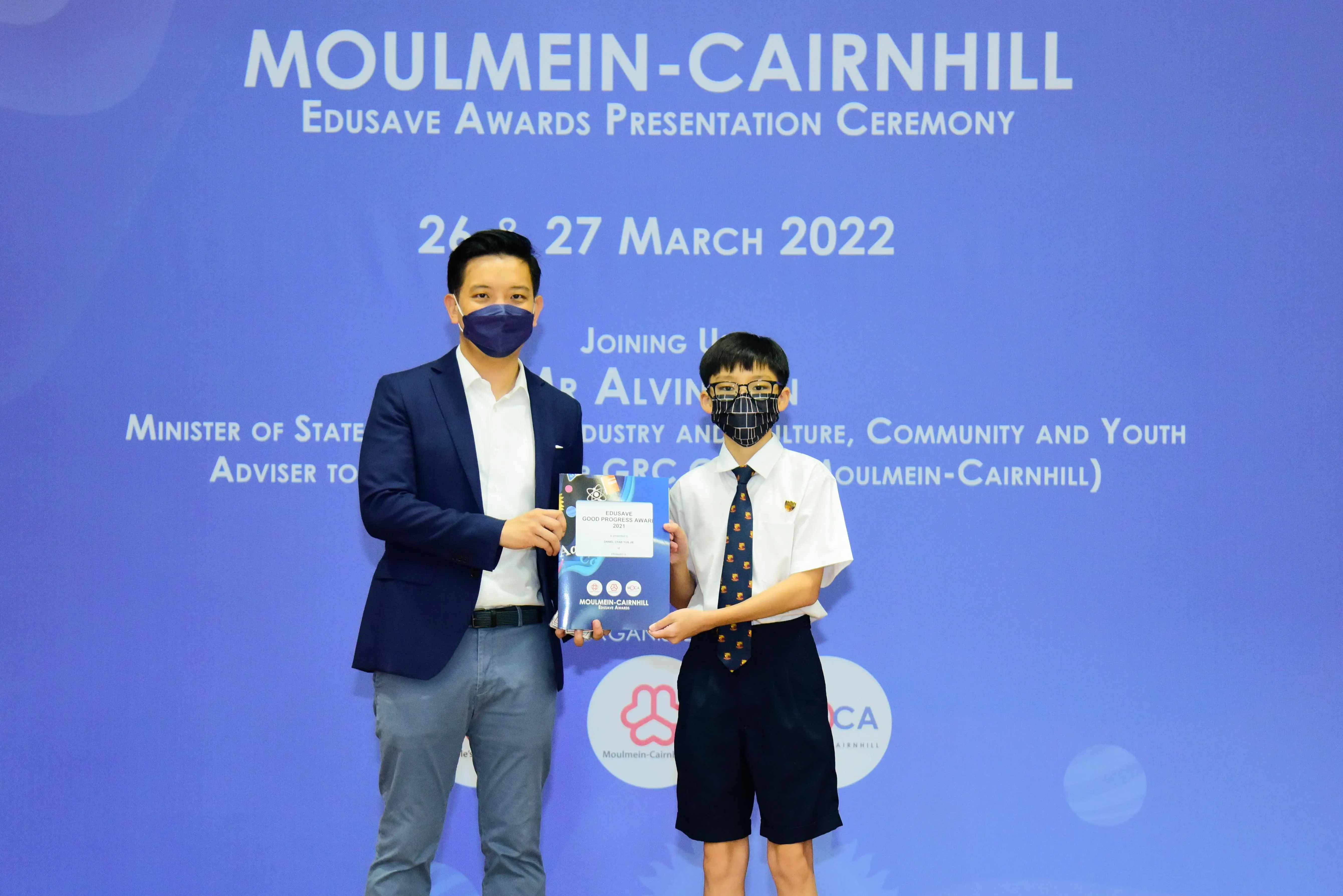 An adult and a young student in uniform hold an award together at the Moulmein-Cairnhill Edusave Awards Ceremony 2022.