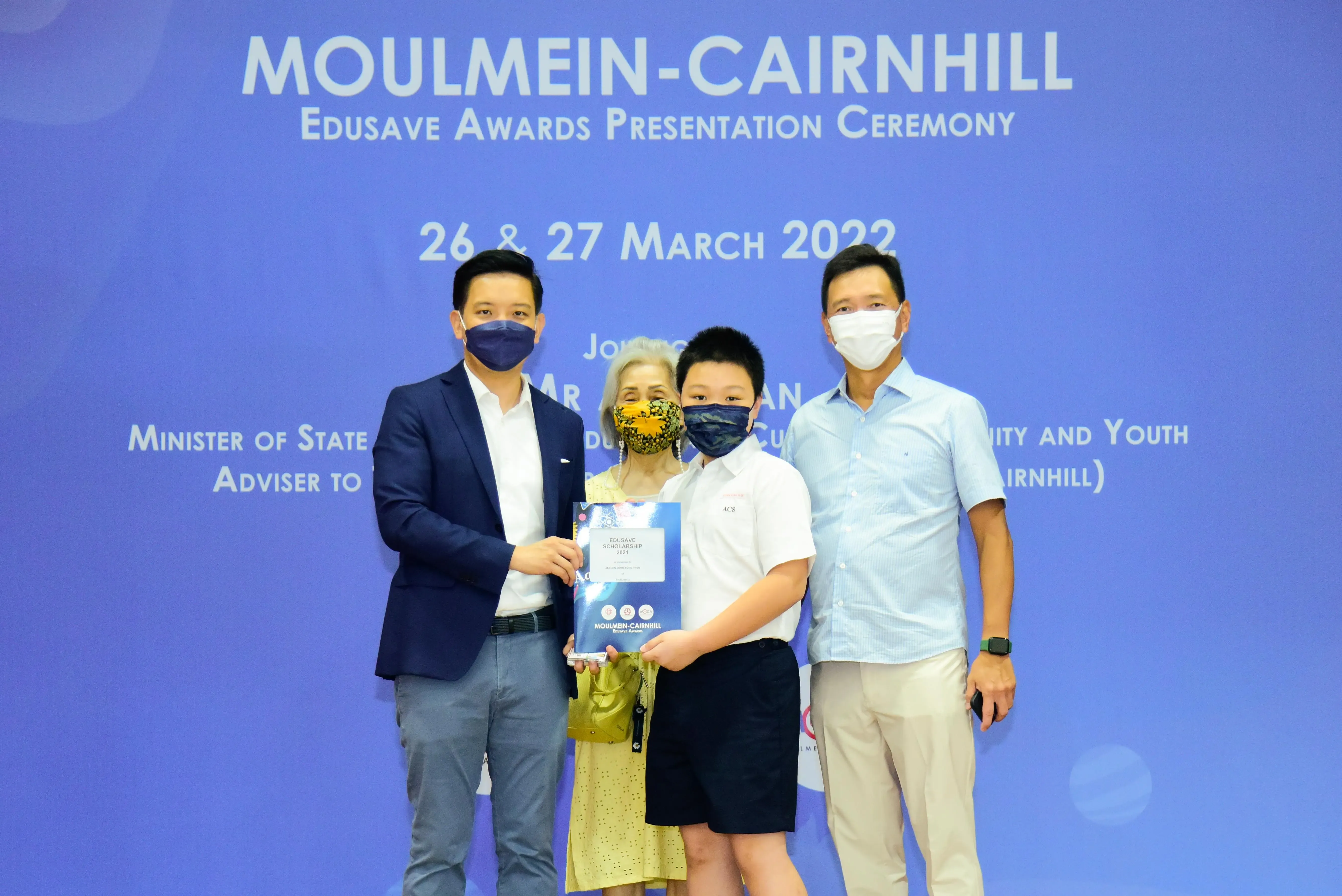 Four masked people pose with an Edusave Scholarship certificate at the Moulmein-Cairnhill Awards Ceremony, March 2022.