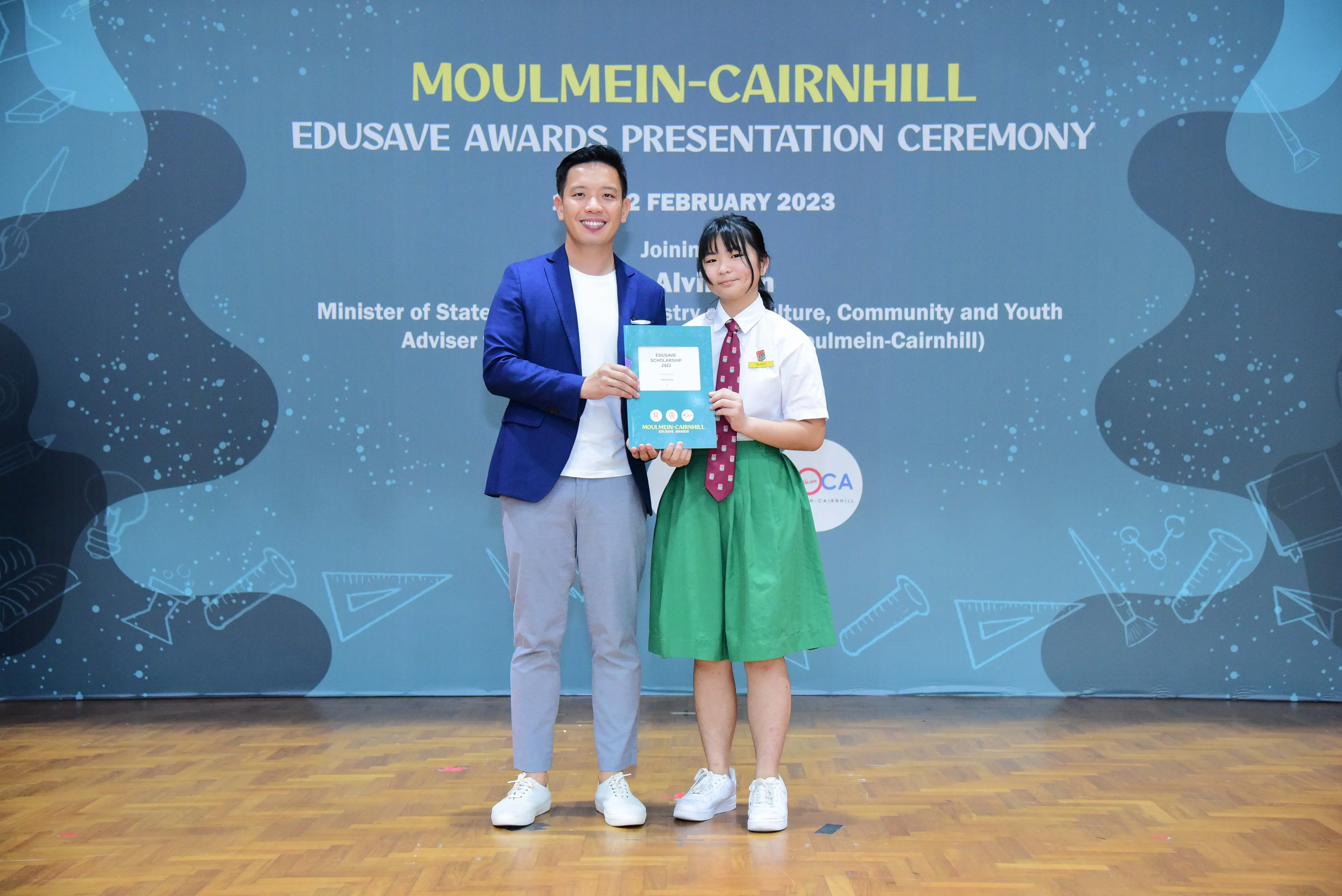 Two people pose holding an award folder at the Moulmein-Cairnhill Edusave Awards Presentation Ceremony, February 2023.
