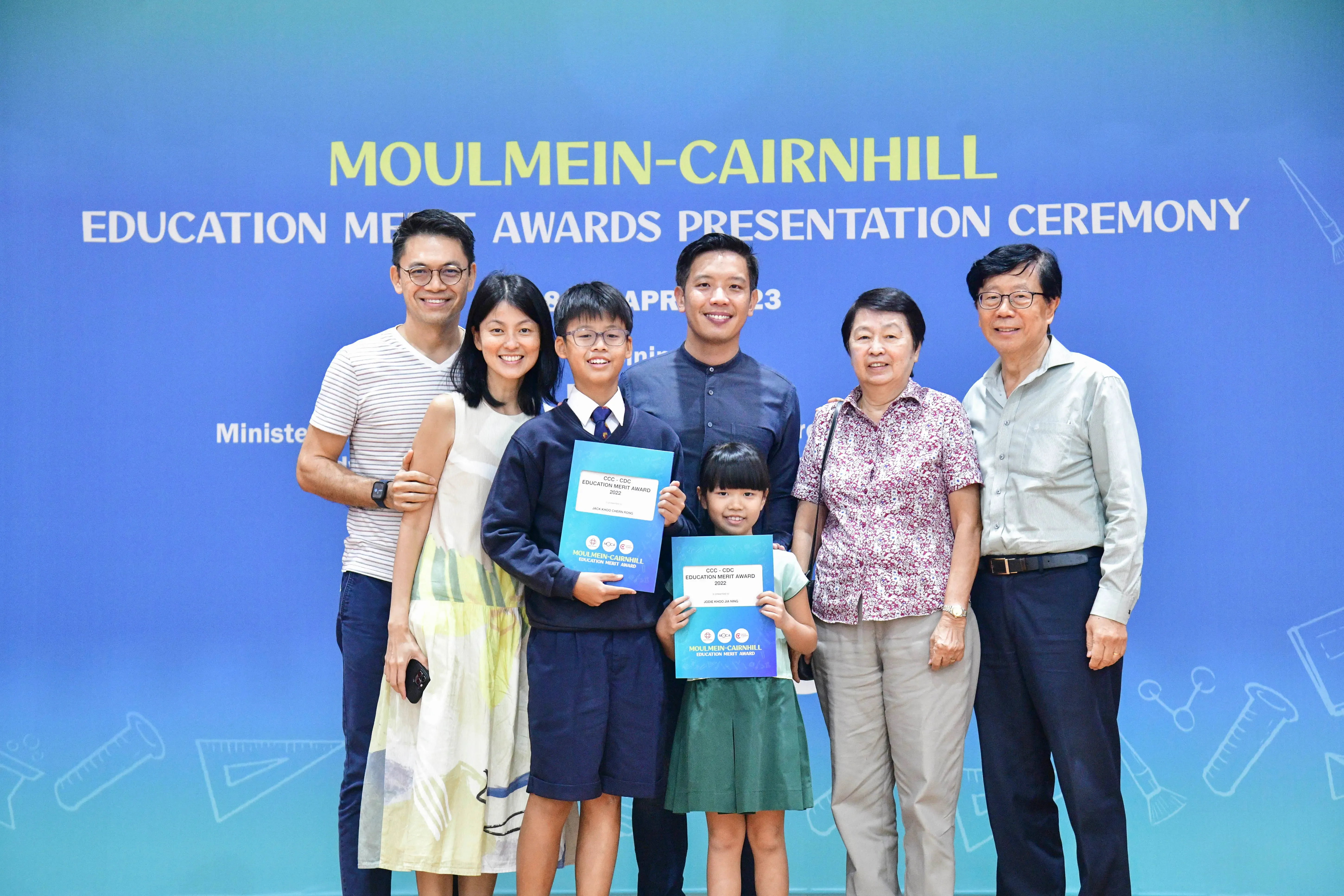 Six adults and two children pose with award certificates at the Moulmein-Cairnhill Education Merit Awards Ceremony.