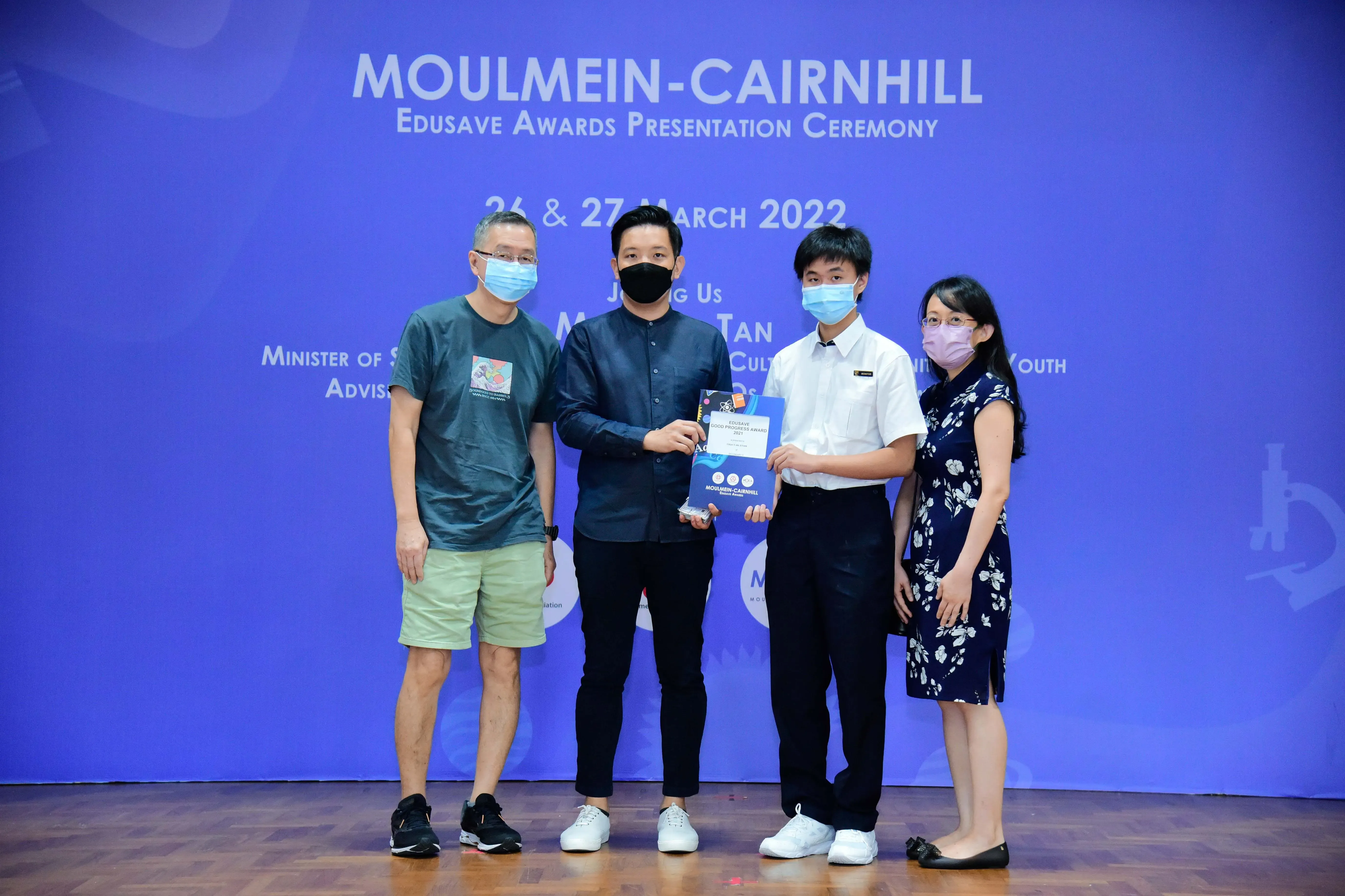 Four masked people stand on a stage at the Moulmein-Cairnhill Edusave Awards Presentation Ceremony, March 2022.
