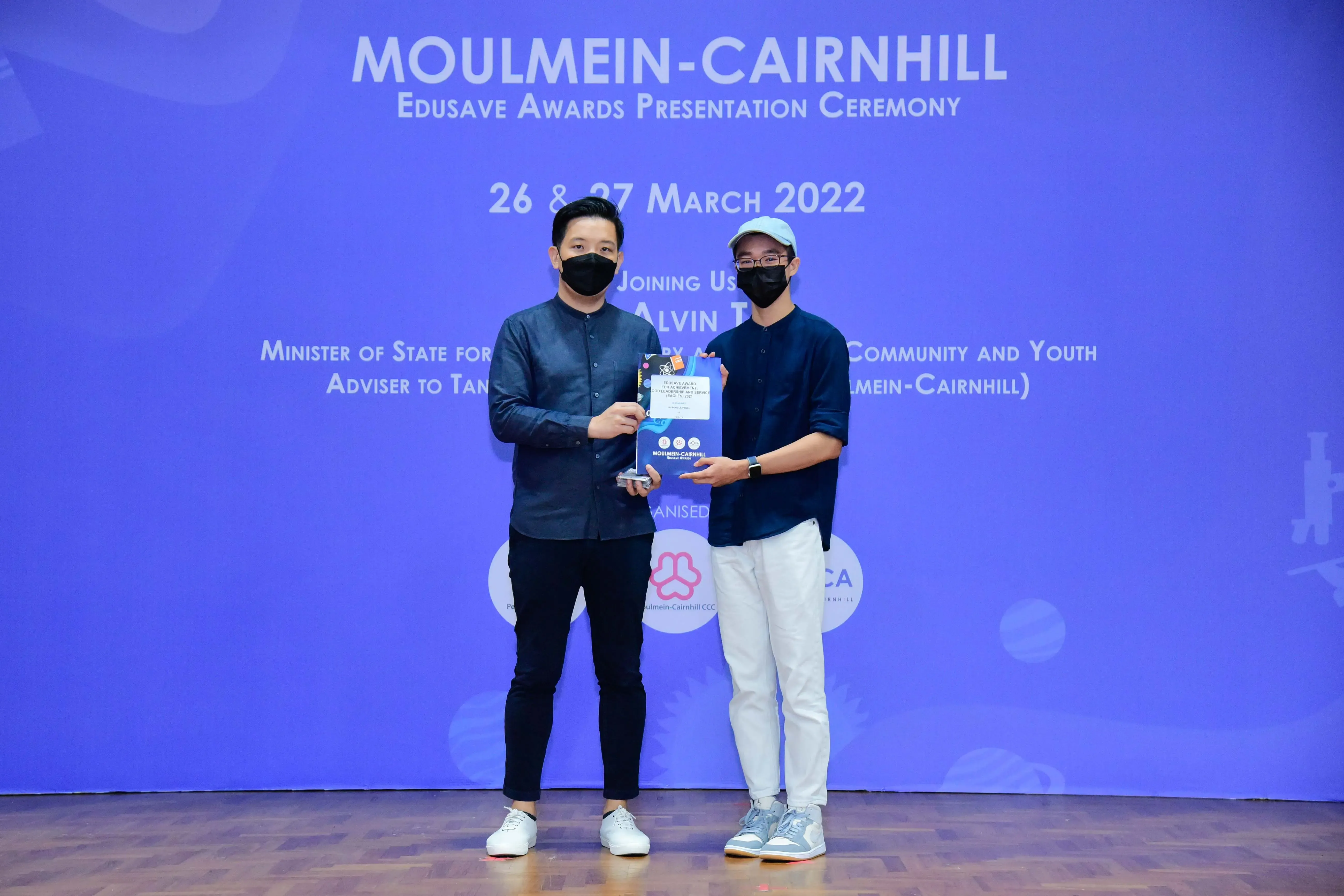 Two masked men hold an award at the Moulmein-Cairnhill Edusave Awards Presentation Ceremony, March 2022.