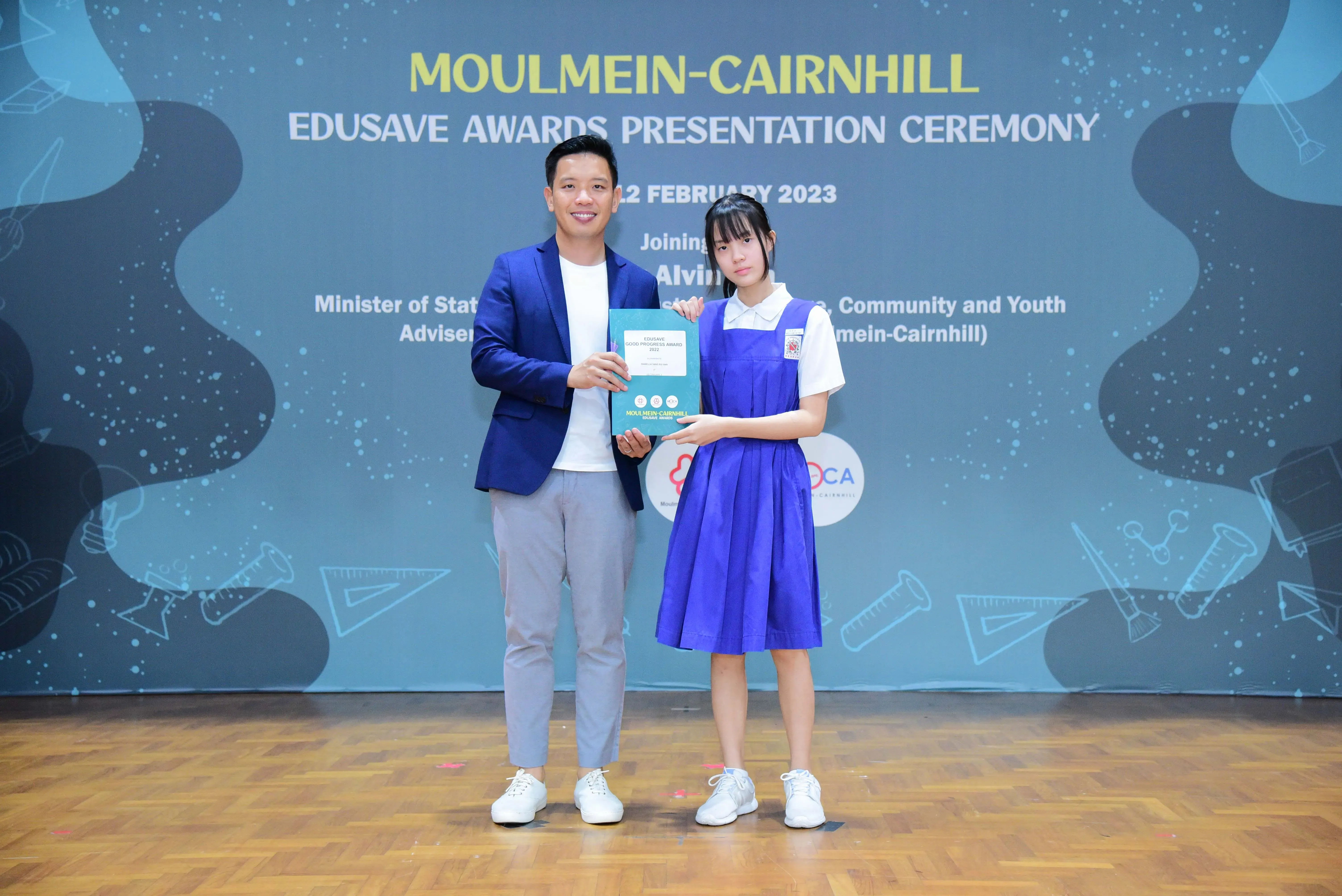 A man and a girl in school uniform hold an award at the Moulmein-Cairnhill Edusave Awards Ceremony, February 2023.