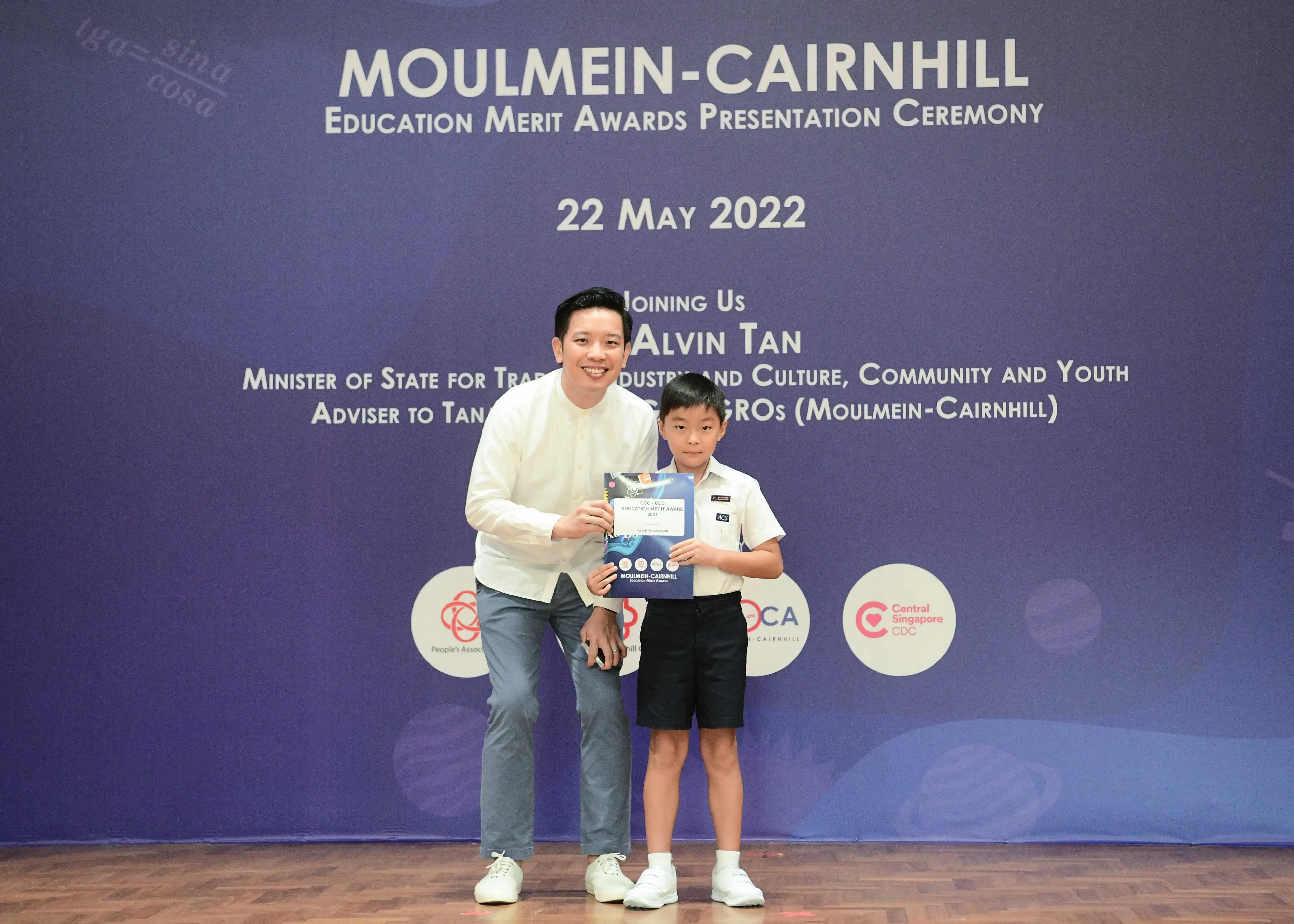 A man and a young boy hold a certificate at the Moulmein-Cairnhill Education Merit Awards on 22 May 2022.