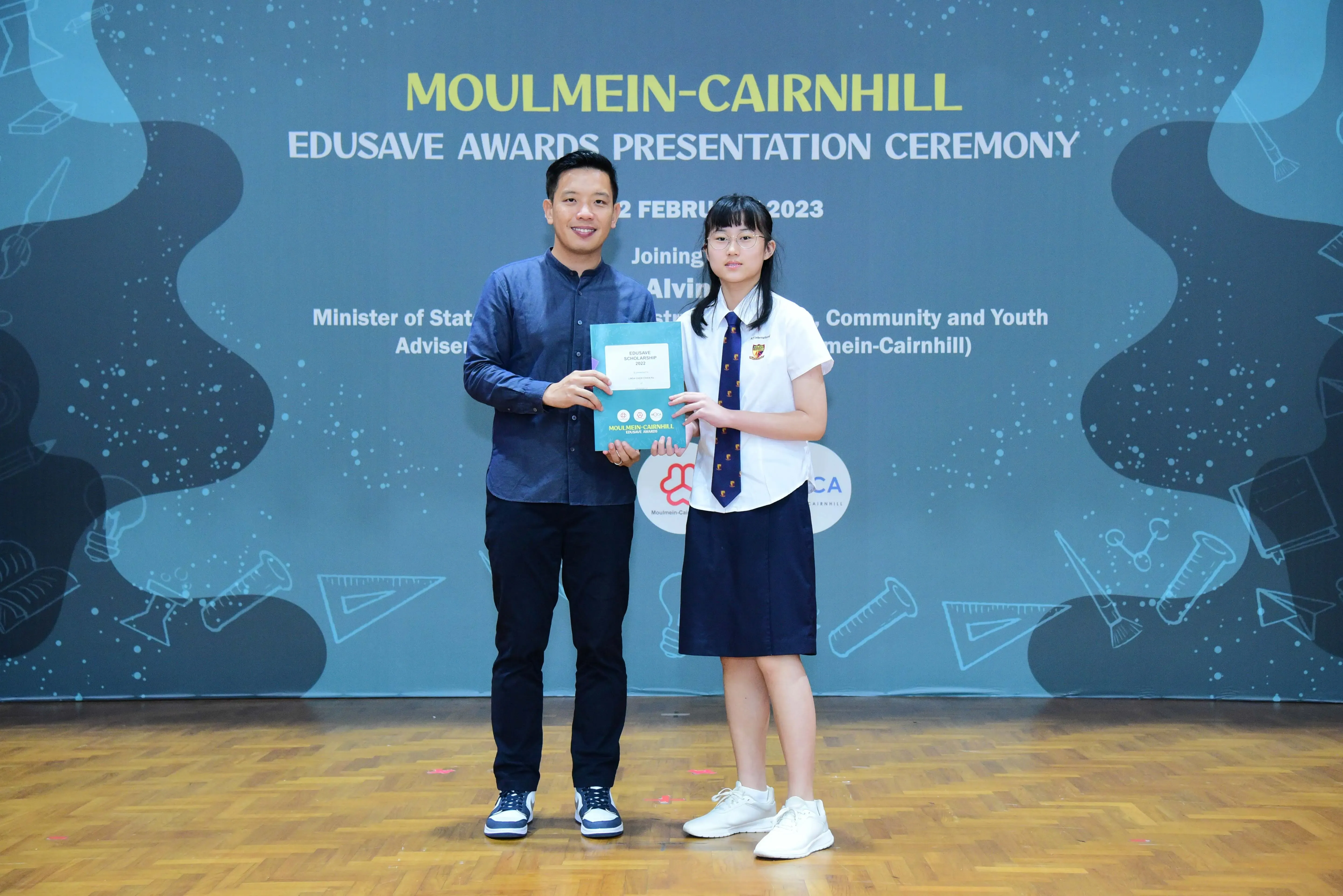 A man and a schoolgirl hold an award certificate at the Moulmein-Cairnhill Edusave Awards Presentation Ceremony 2023.