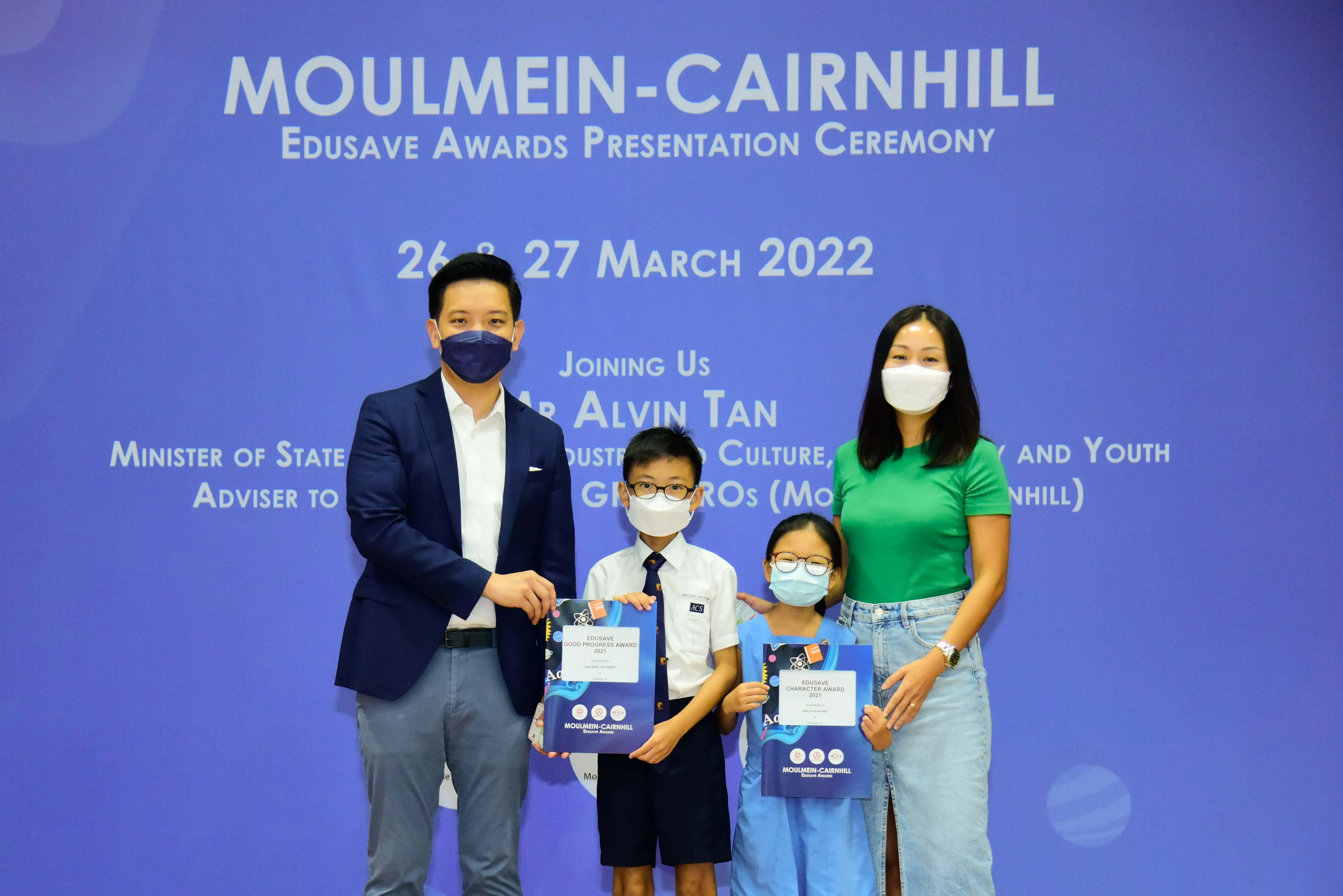 Two adults and two children in masks pose with Edusave awards at the Moulmein-Cairnhill ceremony, March 2022.