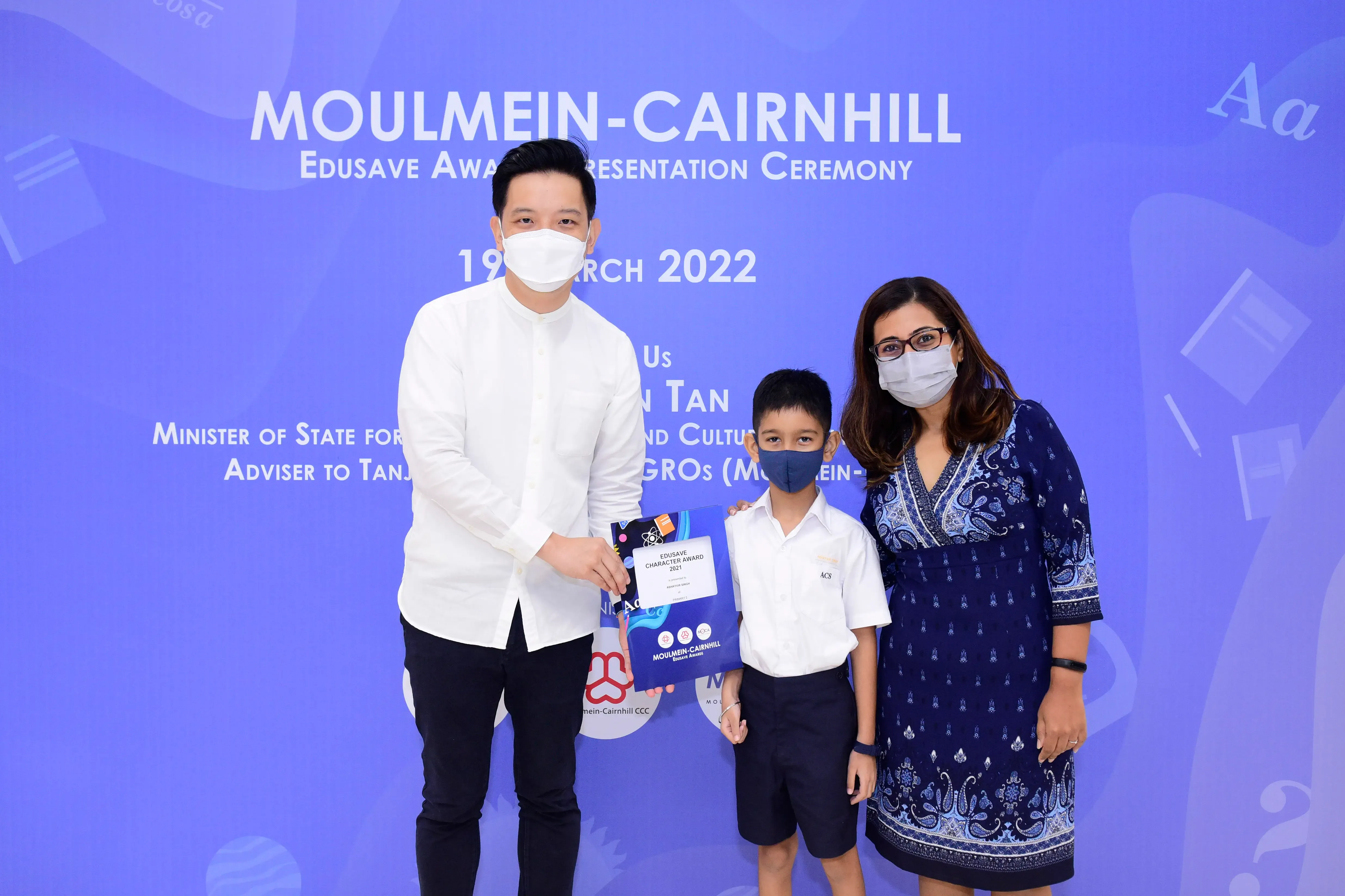 Two masked adults and a masked child pose with an Edusave award certificate at the Moulmein-Cairnhill ceremony.