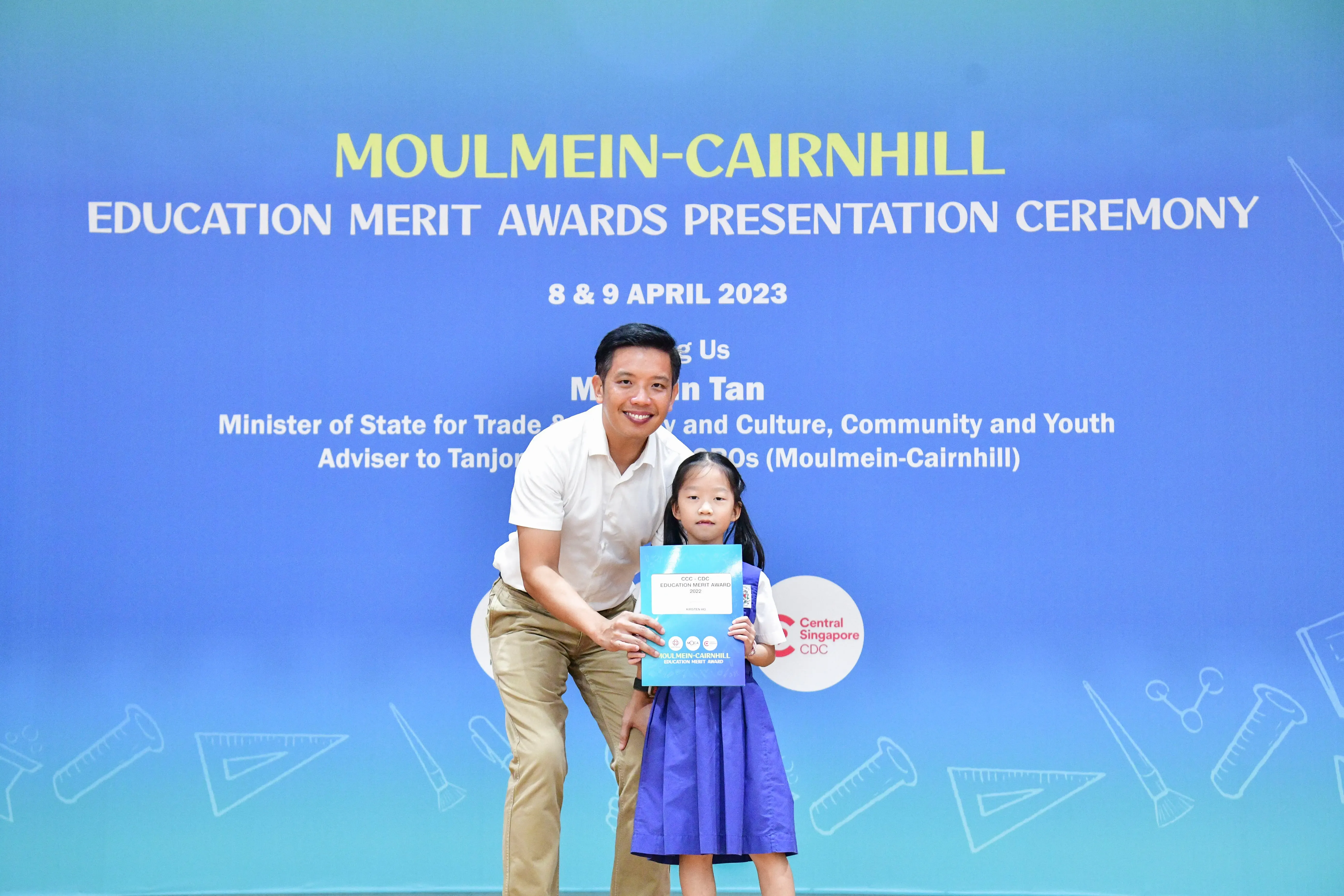 A man and a young girl hold an award certificate at the Moulmein-Cairnhill Education Merit Awards Ceremony, April 2023.