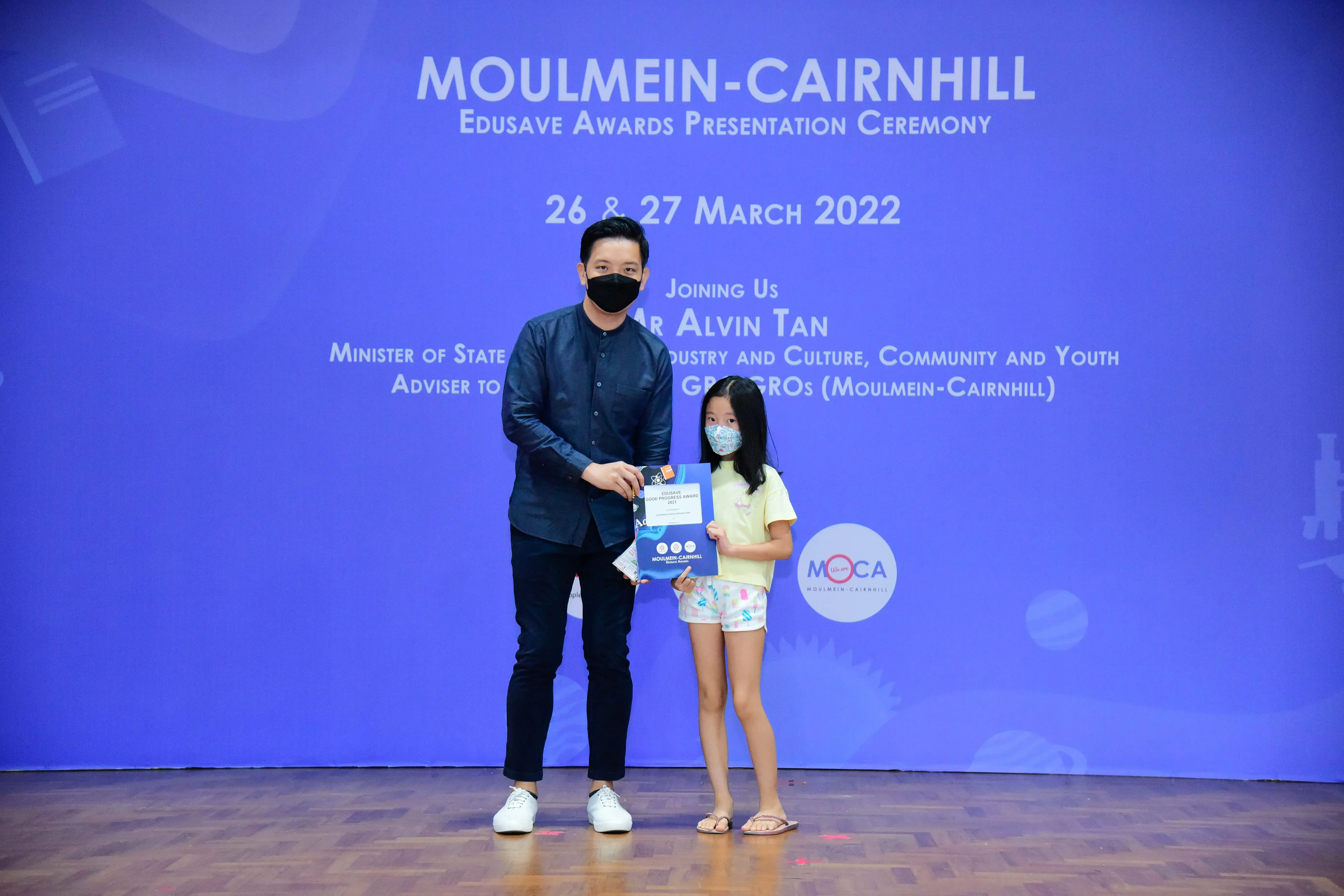 A man and a young girl wearing masks hold a certificate at the Moulmein-Cairnhill Edusave Awards Ceremony, March 2022.