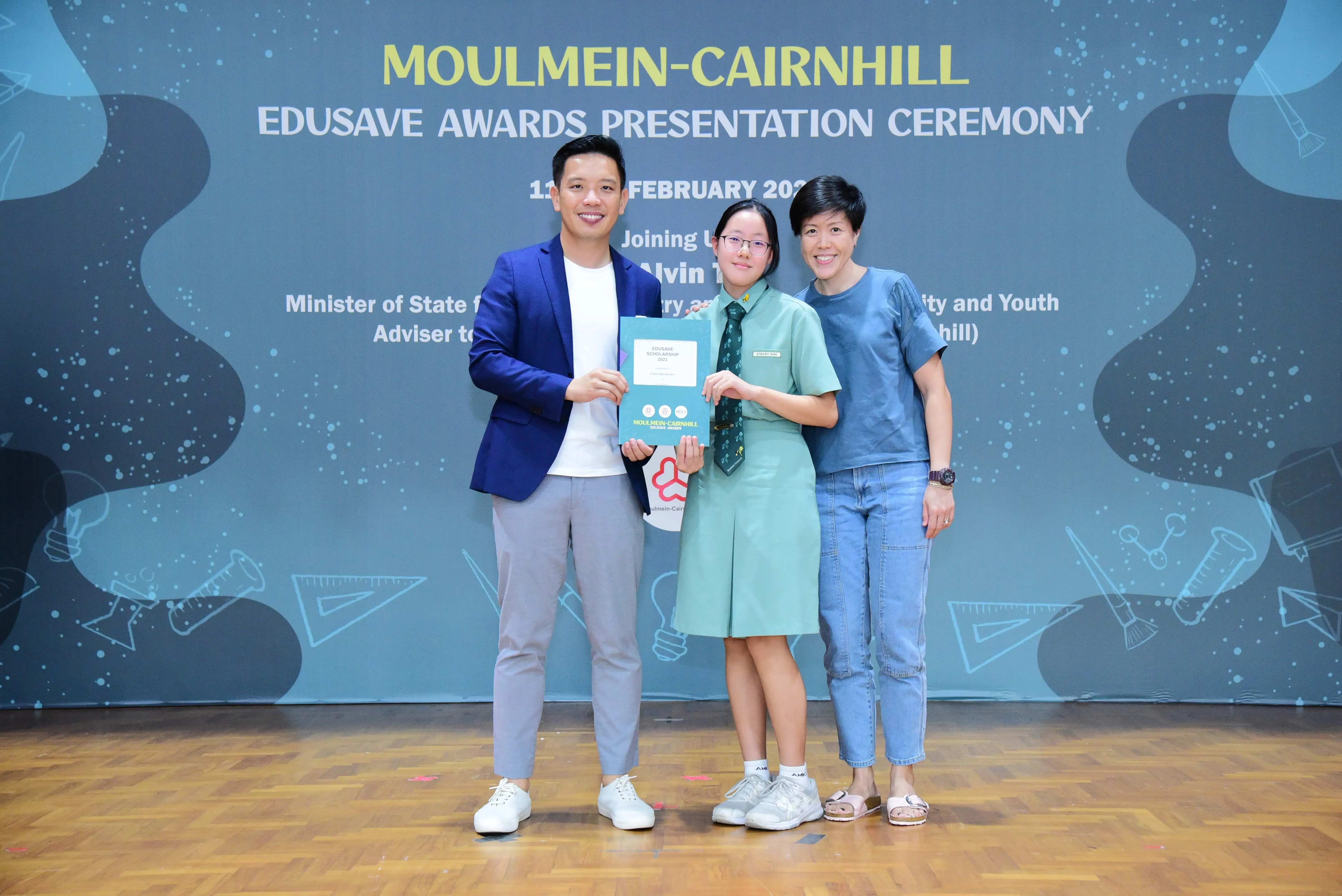 Three people pose at the Moulmein-Cairnhill Edusave Awards Presentation Ceremony, with a student holding an award.