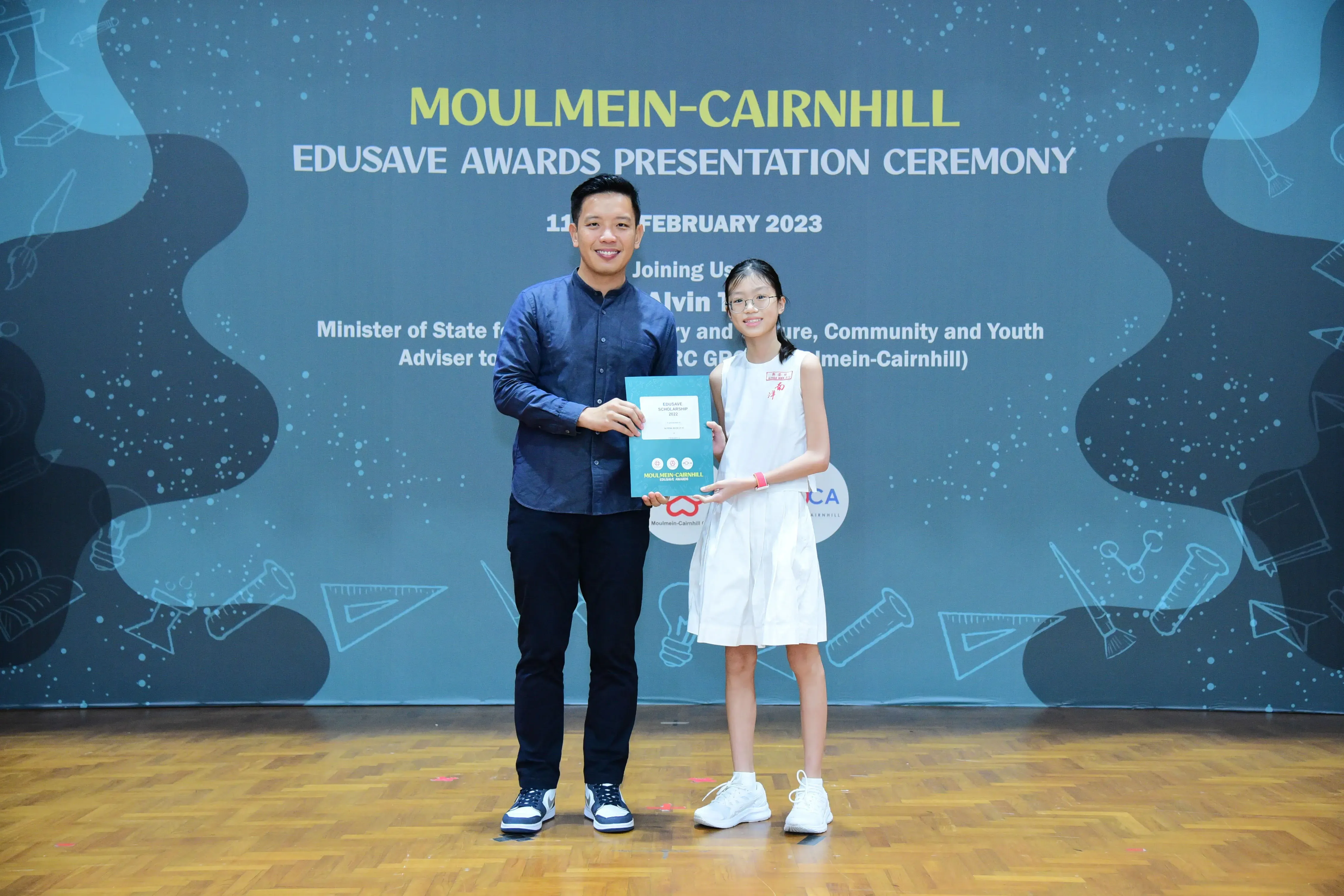 A man and a young girl hold an award certificate at the Moulmein-Cairnhill Edusave Awards Presentation Ceremony 2023.