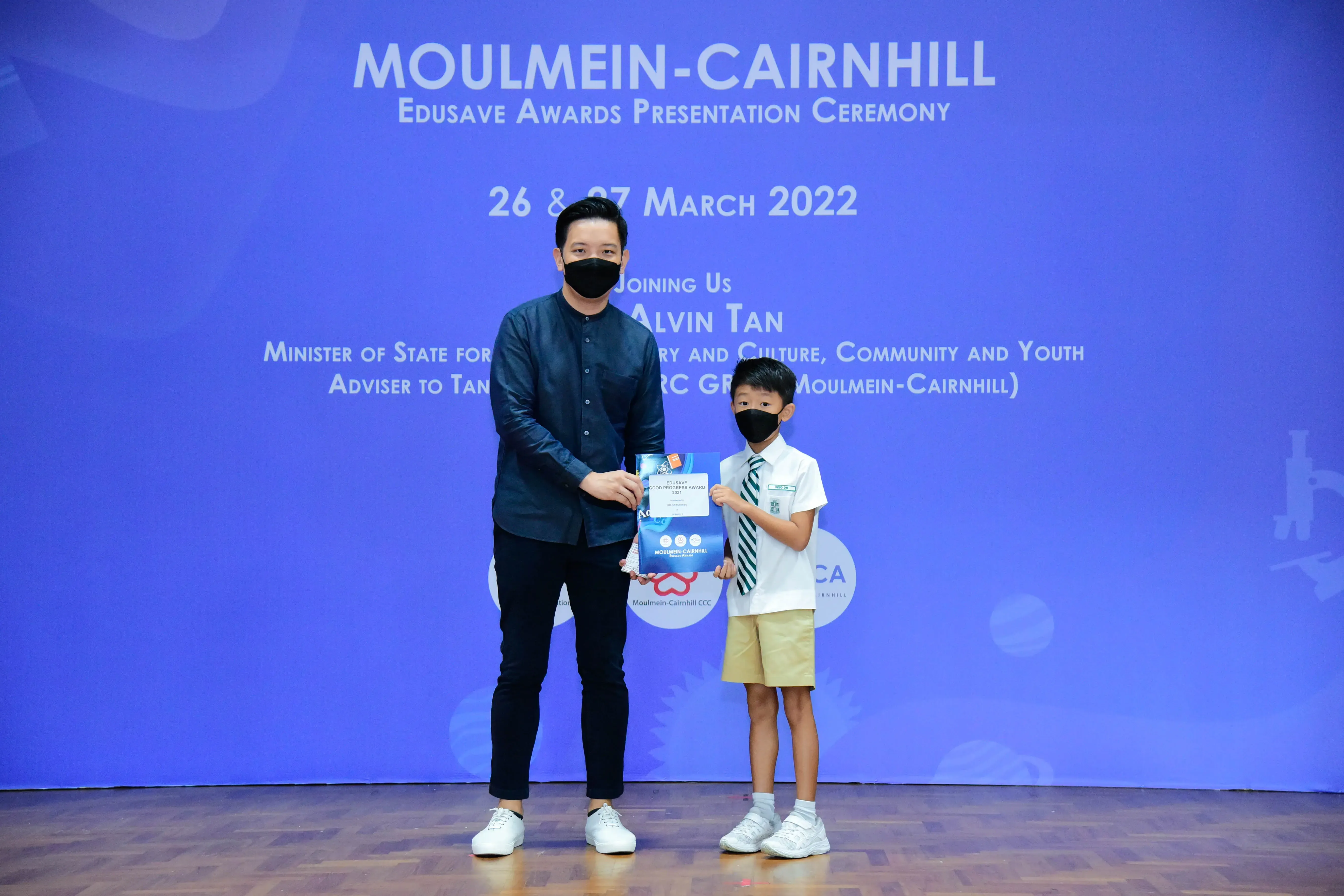 An adult and a young student in uniform hold an award at the Moulmein-Cairnhill Edusave Awards Ceremony, March 2022.