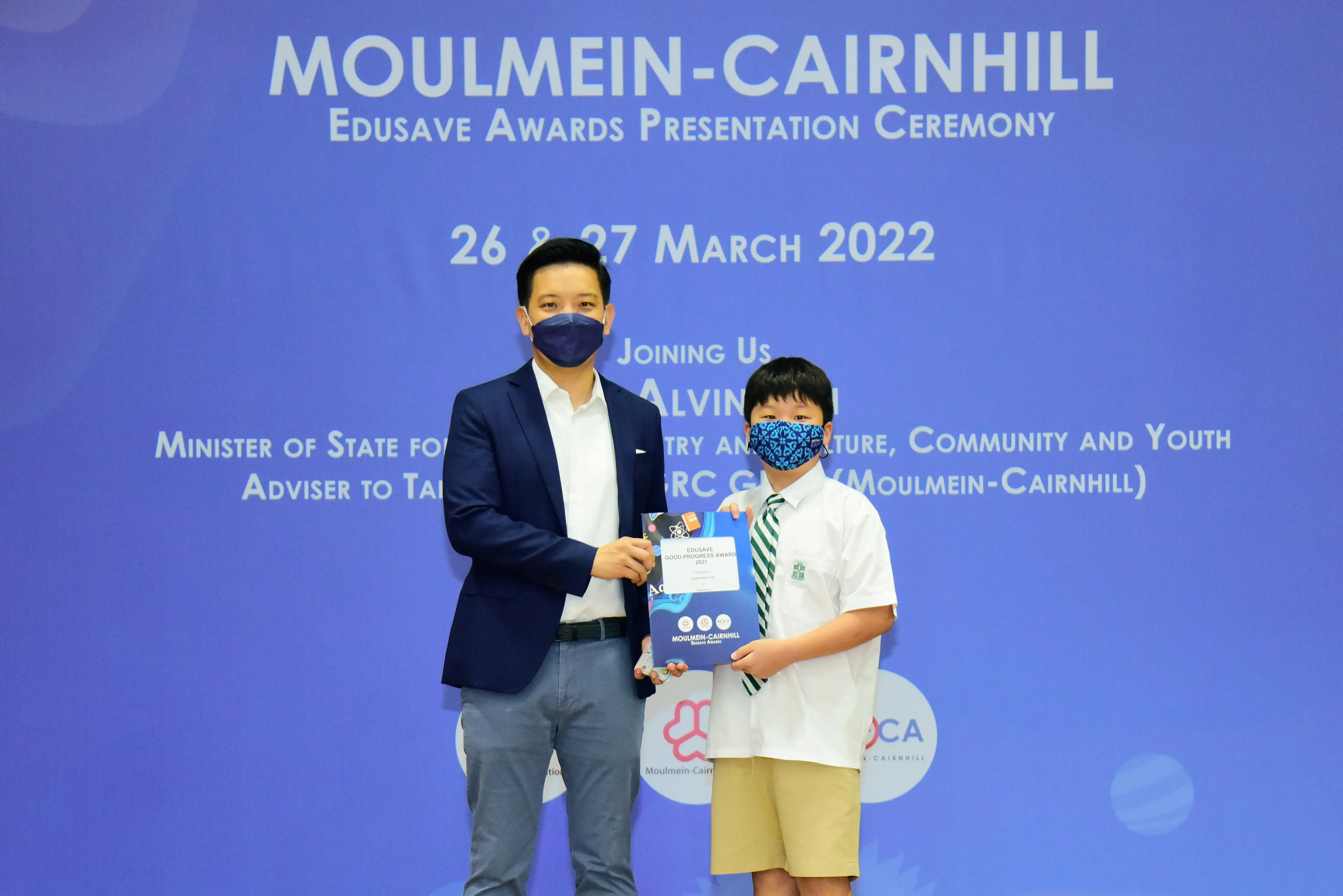 An adult and a child wearing masks hold an award at the Moulmein-Cairnhill Edusave Awards Ceremony, March 2022.