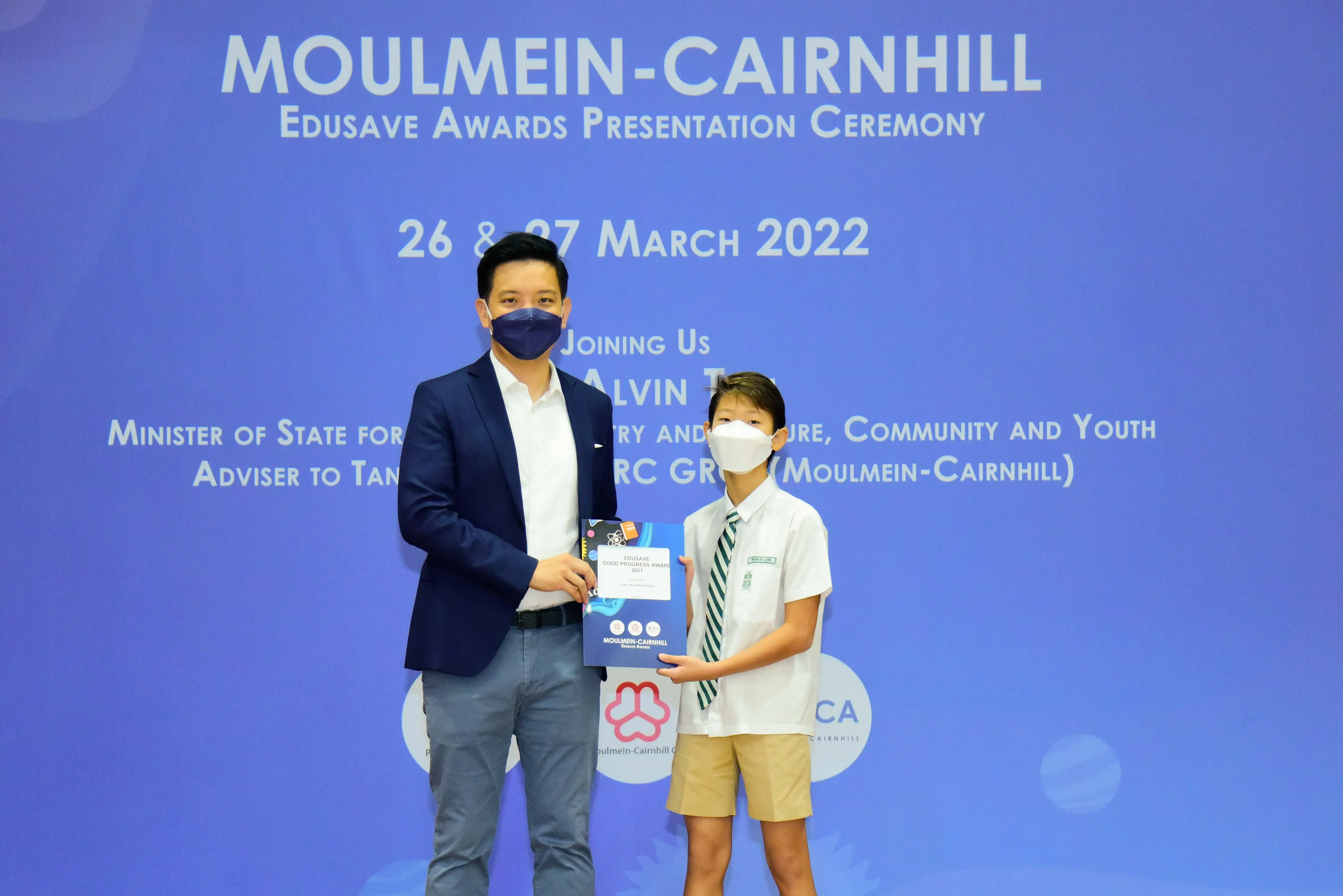 An adult and a student in school uniform hold an award at the Moulmein-Cairnhill Edusave Awards Ceremony, March 2022.