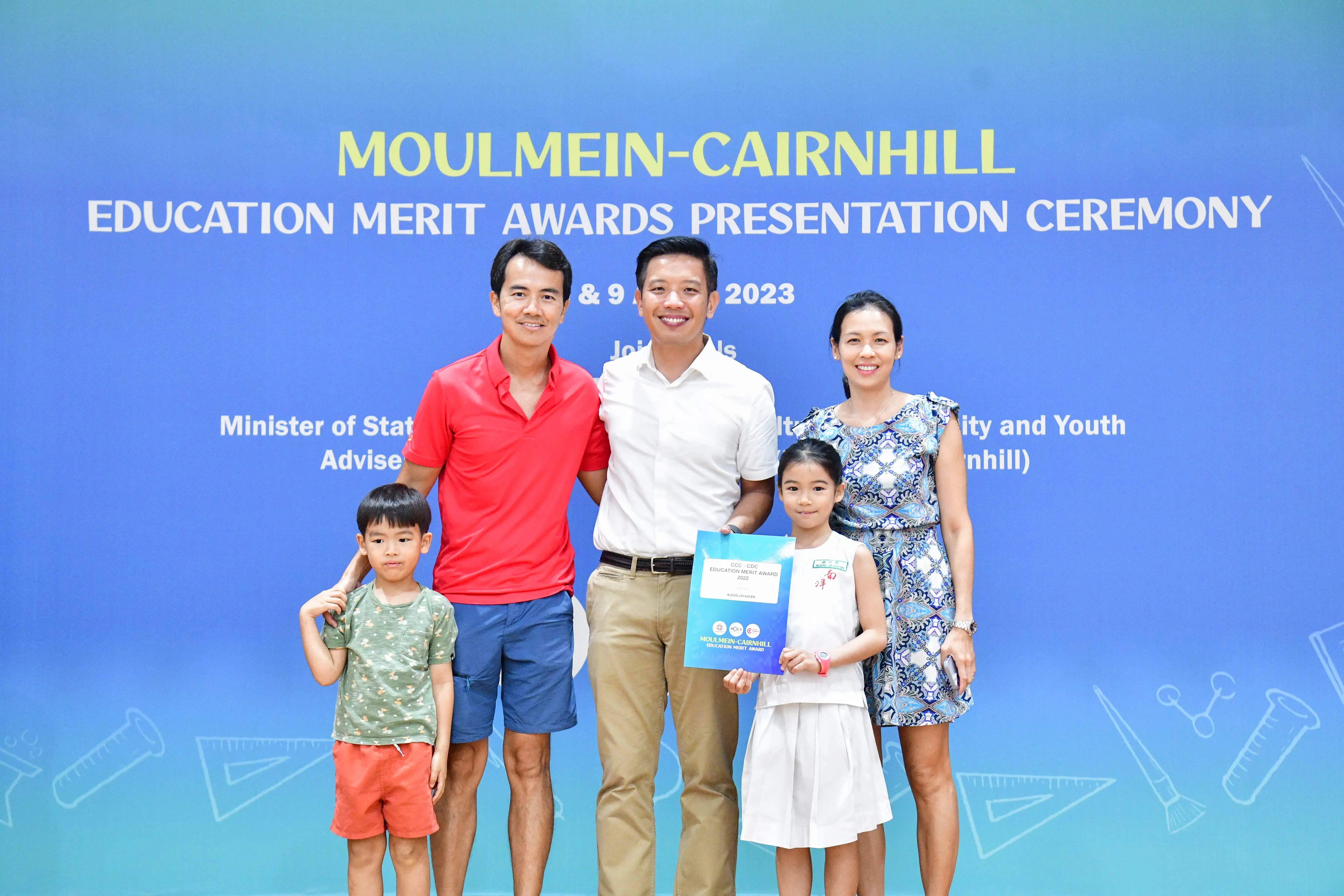 Five people pose at the 2023 Moulmein-Cairnhill Education Merit Awards Ceremony, including a girl holding an award certificate.