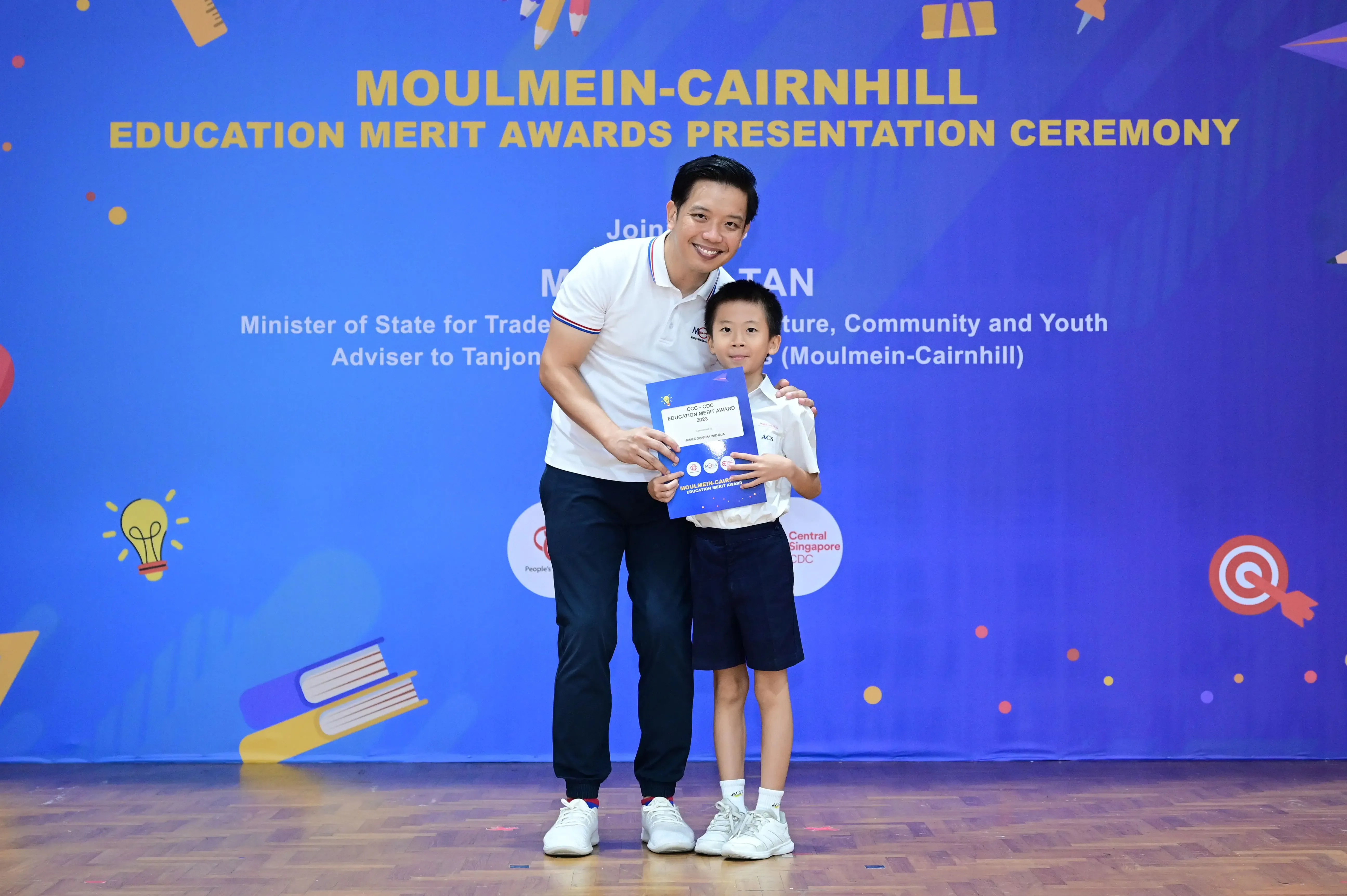 A man and a young boy hold a certificate at the Moulmein-Cairnhill Education Merit Awards Presentation Ceremony.