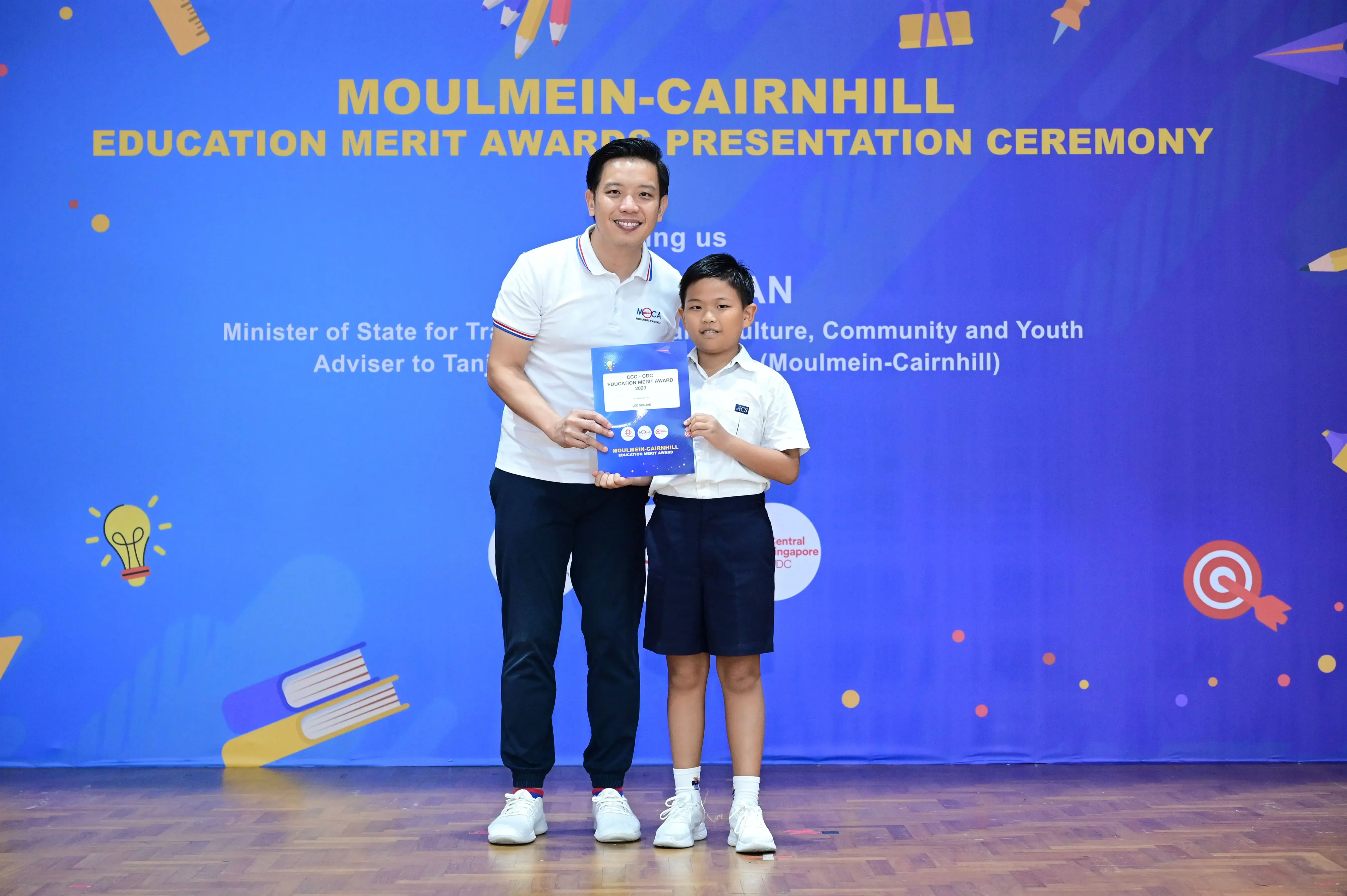 A man and a young boy hold a certificate together at the Moulmein-Cairnhill Education Merit Awards Presentation Ceremony.