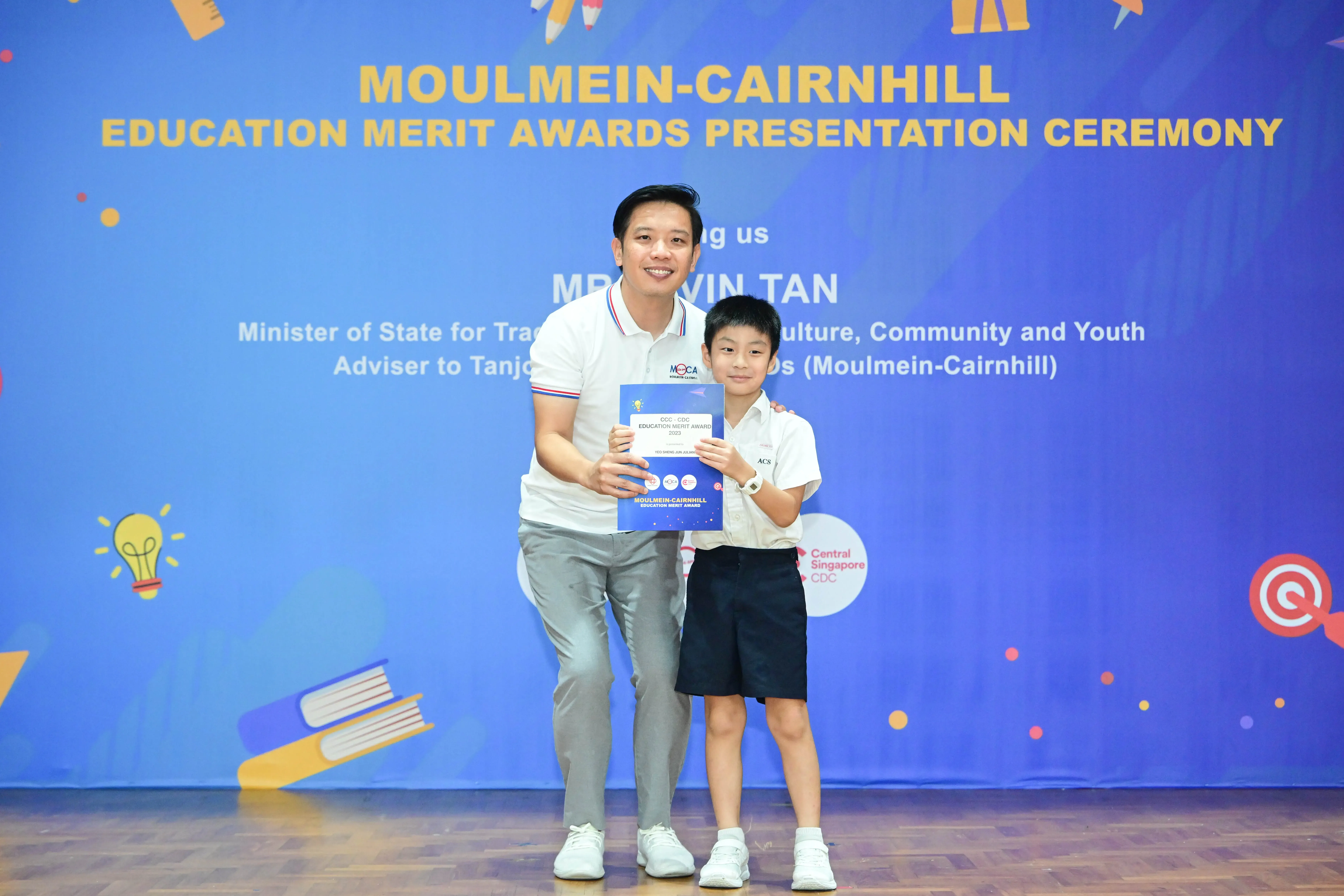A man and a young boy hold an award certificate at the Moulmein-Cairnhill Education Merit Awards Presentation Ceremony.