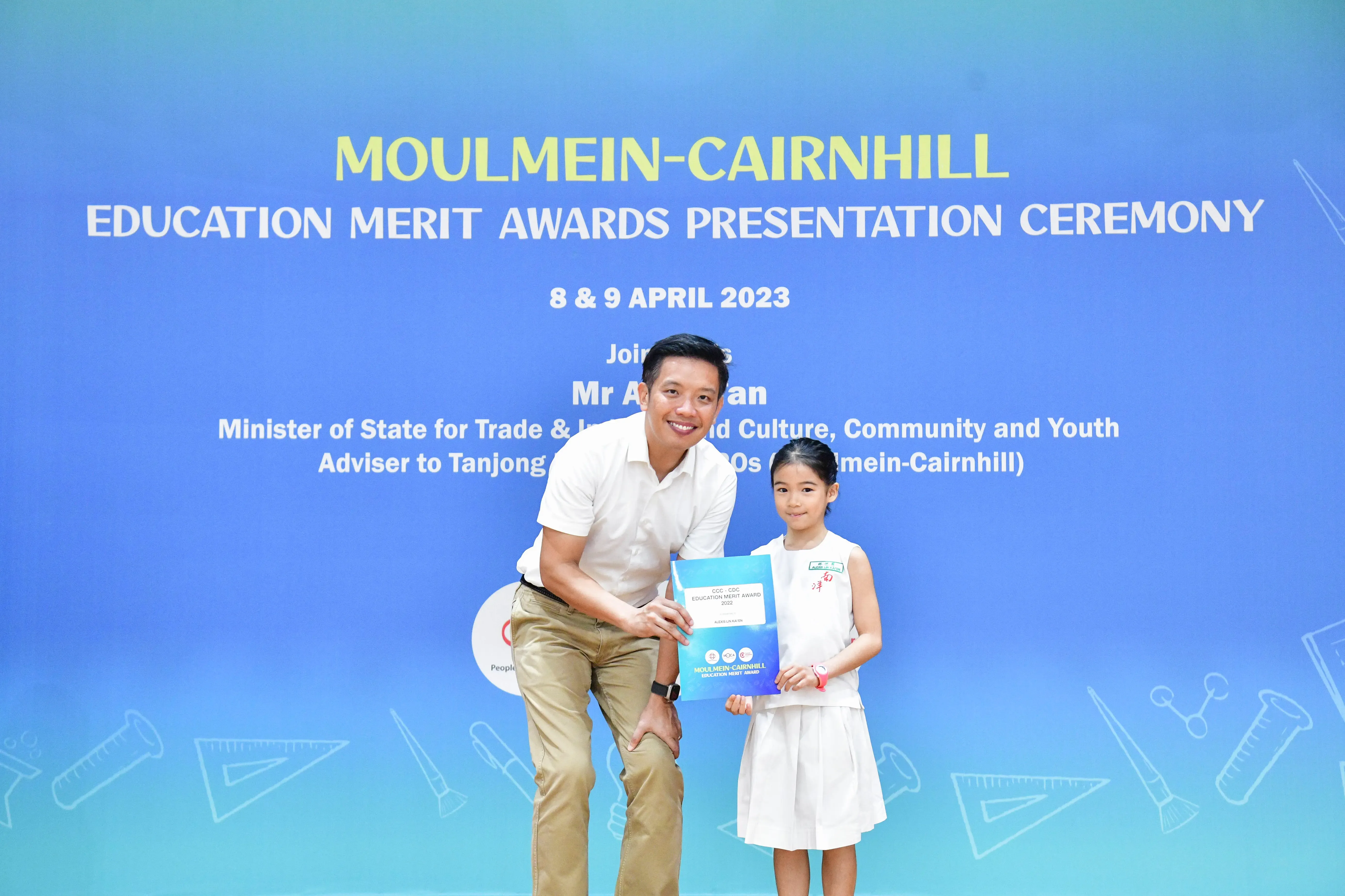 A man and a young girl pose holding an award certificate at the Moulmein-Cairnhill Education Merit Awards ceremony.