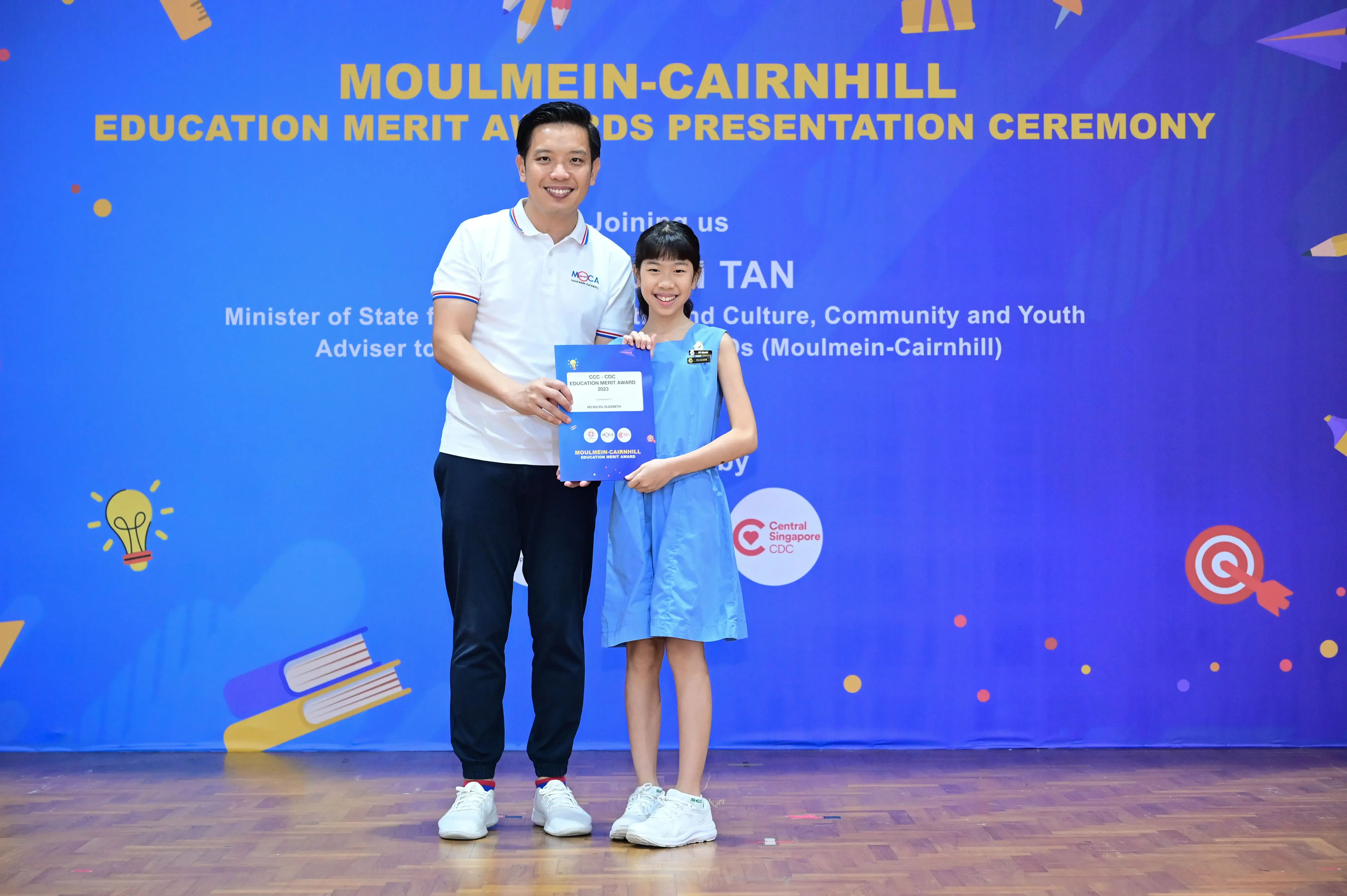 A man and a young girl hold a certificate at the Moulmein-Cairnhill Education Merit Awards Presentation Ceremony.