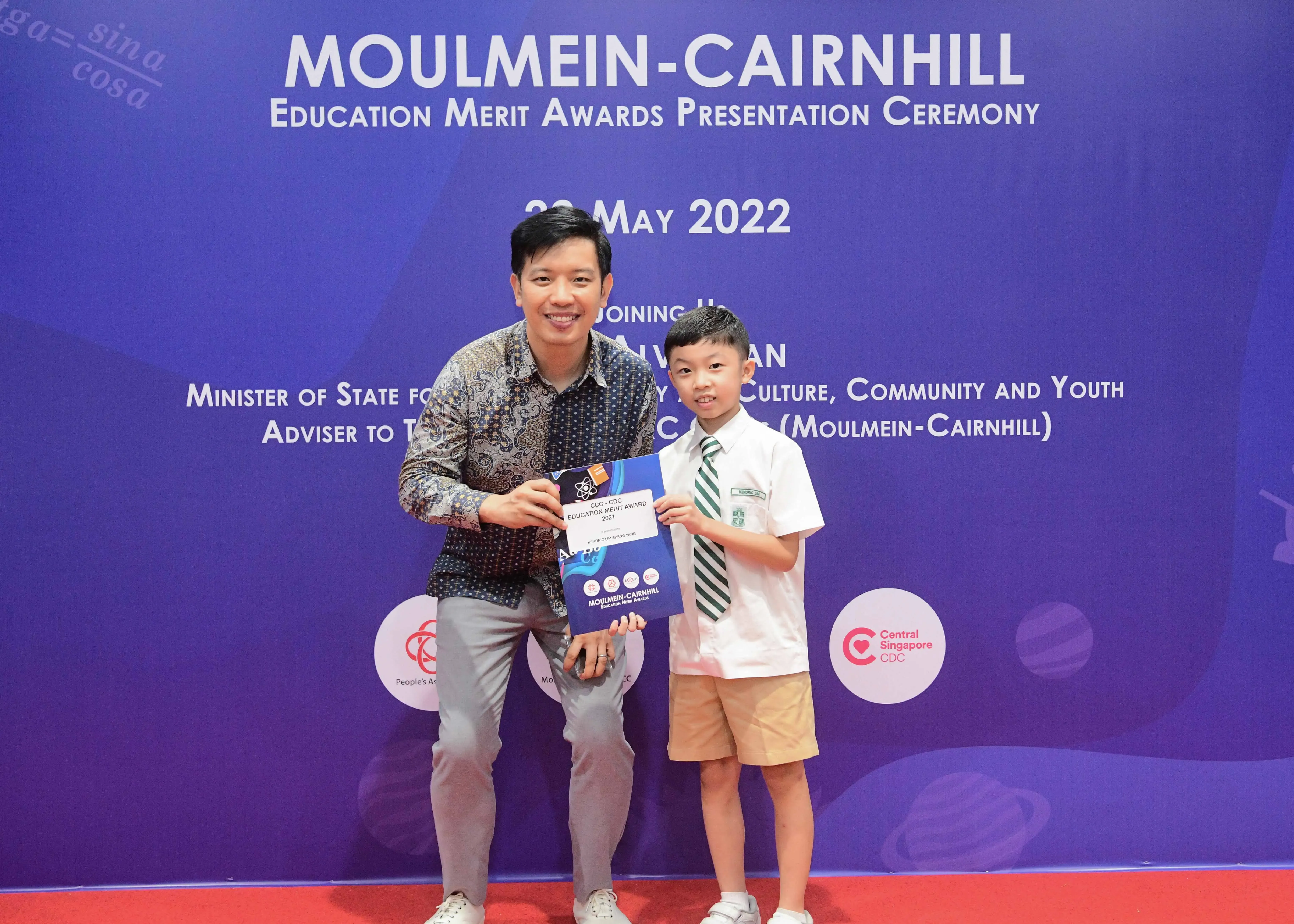 A man and a young boy hold an award certificate at the Moulmein-Cairnhill Education Merit Awards Ceremony, May 2022.