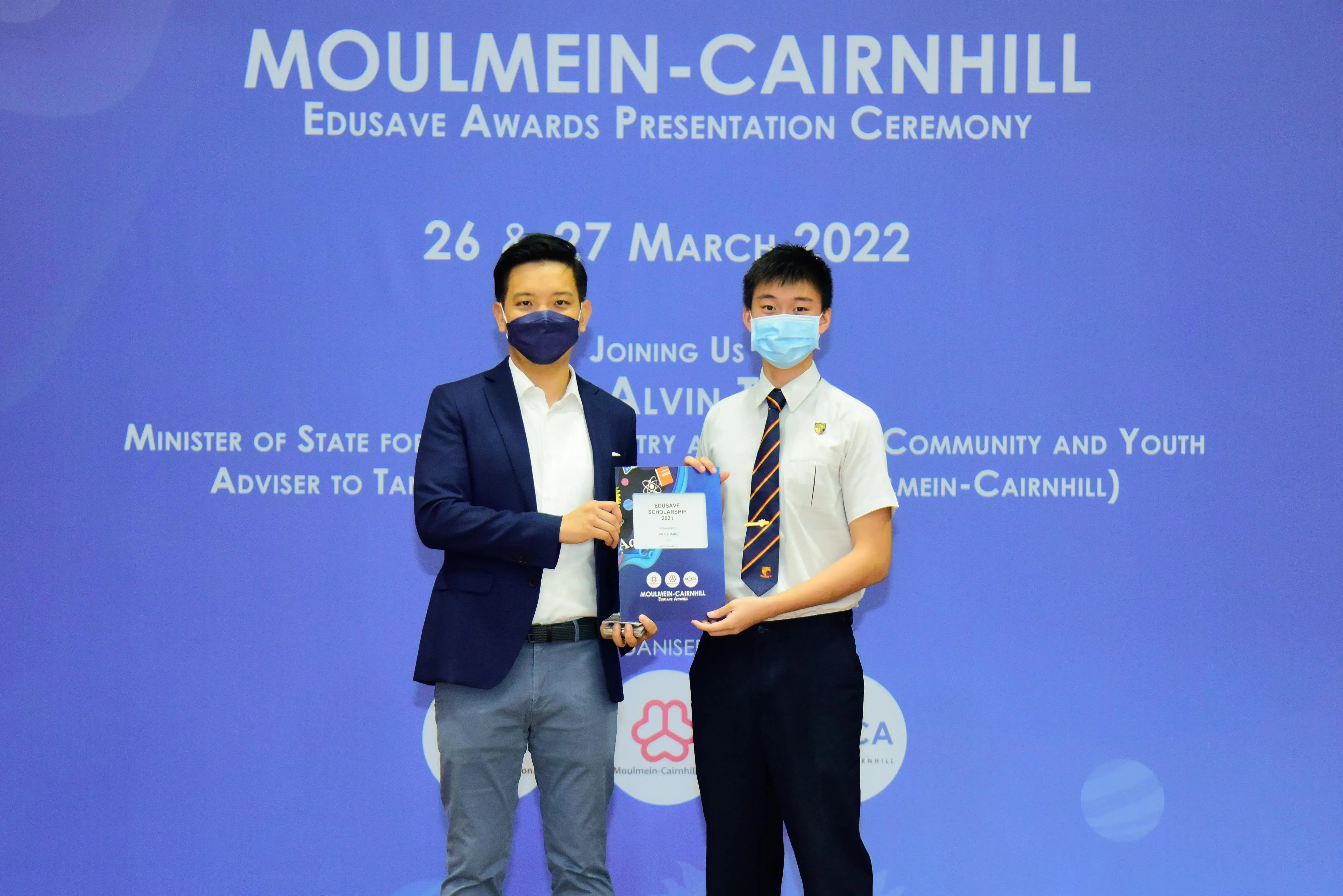 Two masked individuals hold an award booklet at the Moulmein-Cairnhill Edusave Awards Ceremony, March 2022.