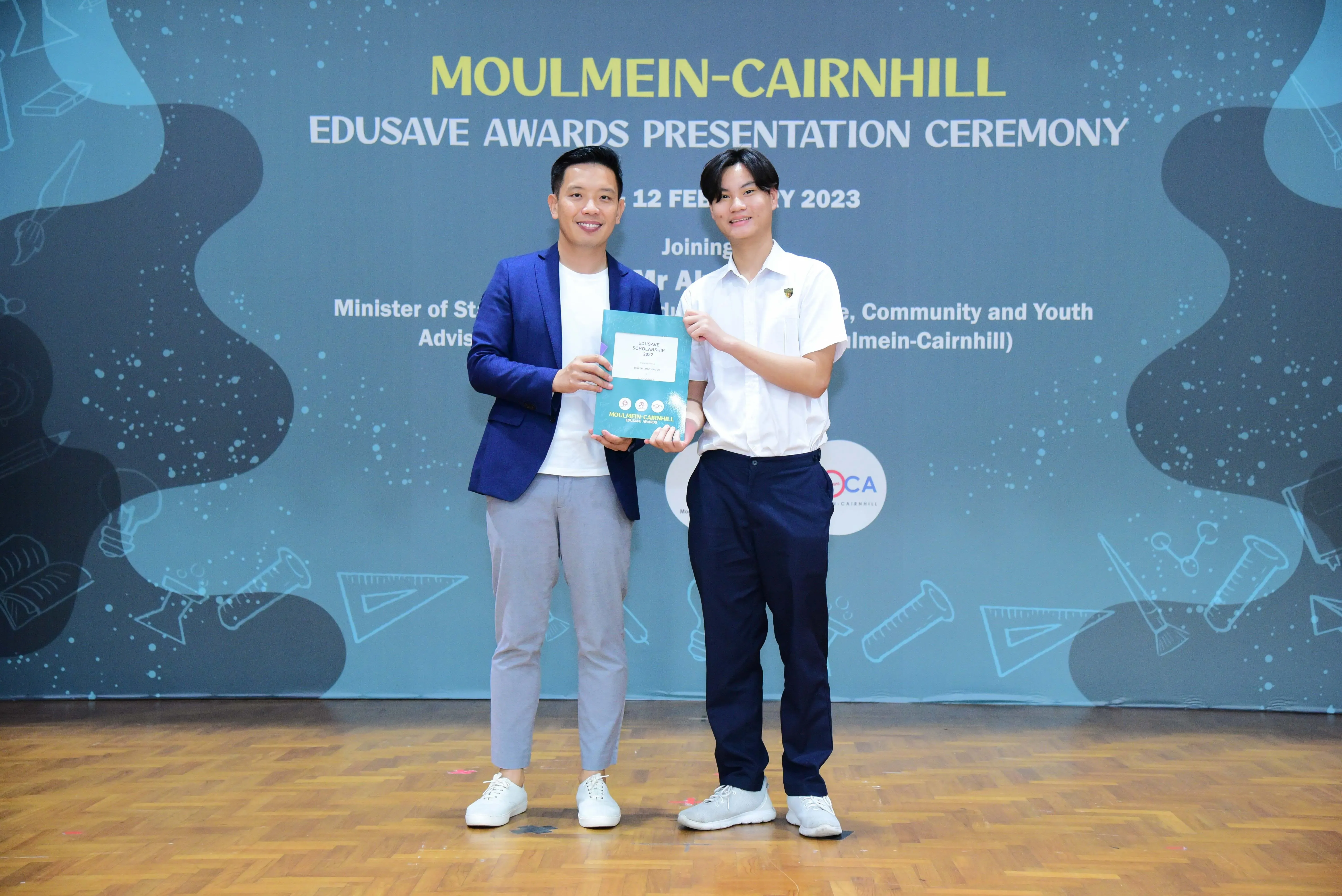 Two men pose holding an award booklet at the Moulmein-Cairnhill Edusave Awards Presentation Ceremony, February 2023.