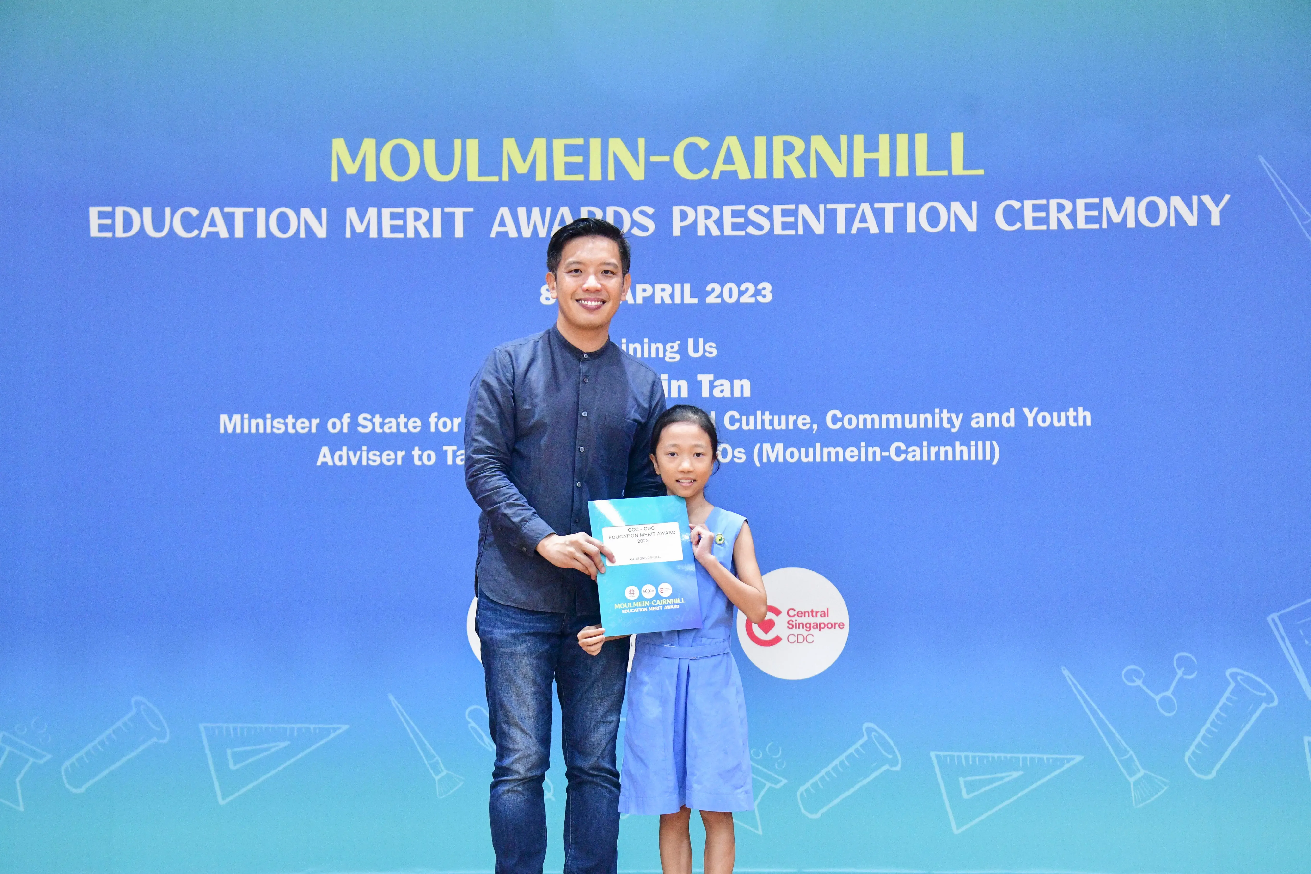 A man and a young girl hold an award certificate at the Moulmein-Cairnhill Education Merit Awards Ceremony, April 2023.