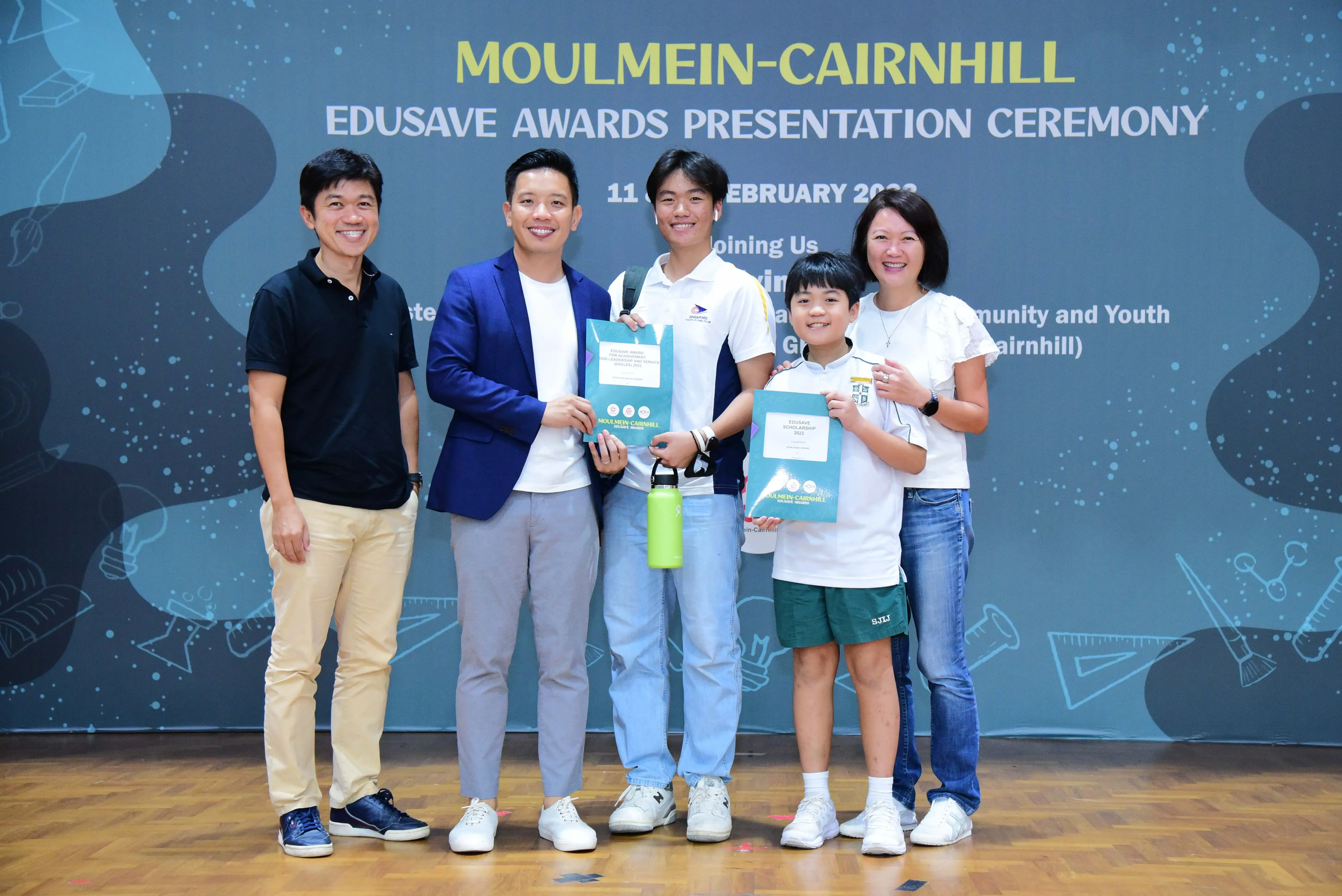 Five people pose holding award booklets at the Moulmein-Cairnhill Edusave Awards Presentation Ceremony.