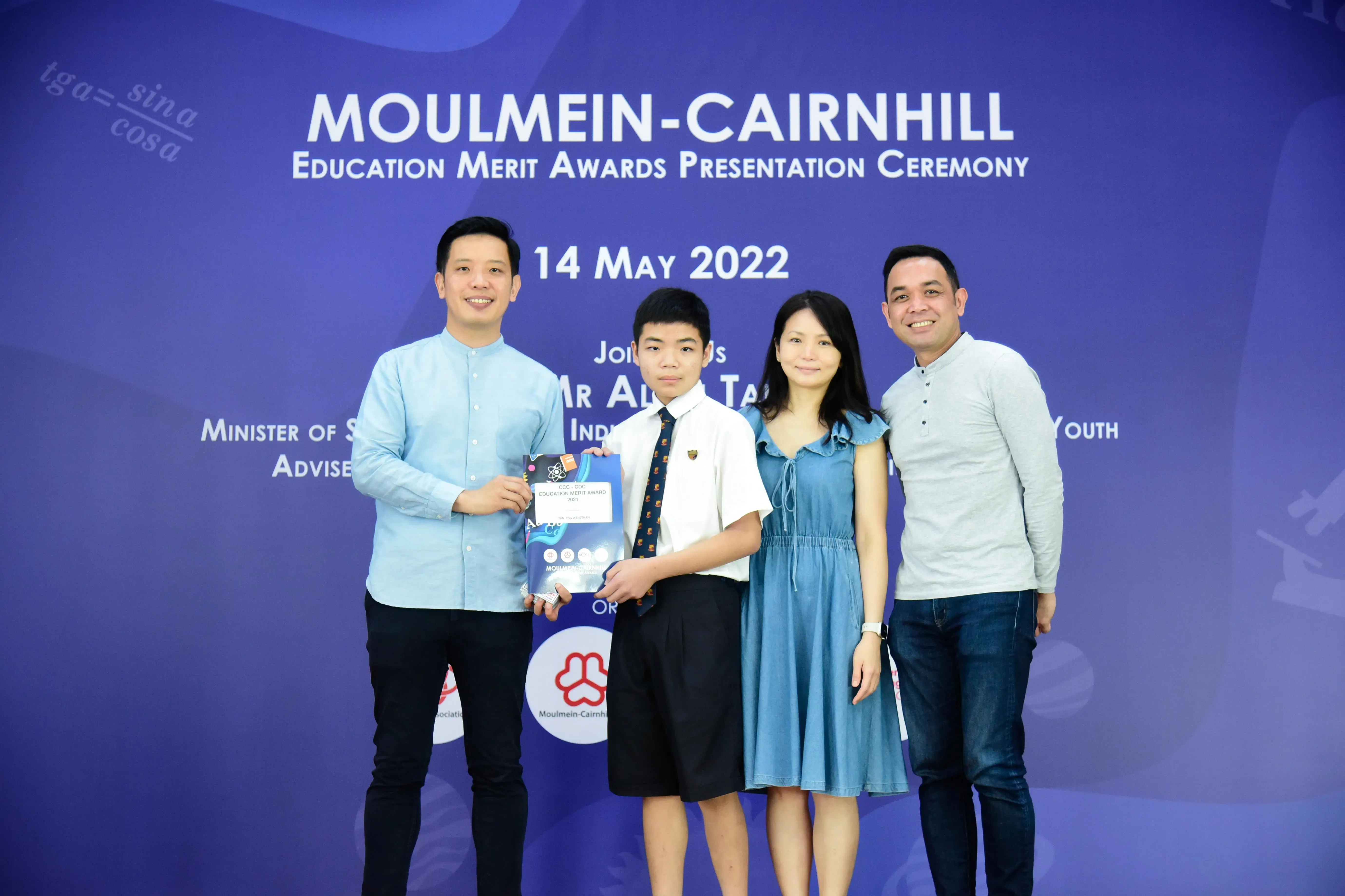 Four people pose at the Moulmein-Cairnhill Education Merit Awards ceremony on 14 May 2022, with a boy holding an award.