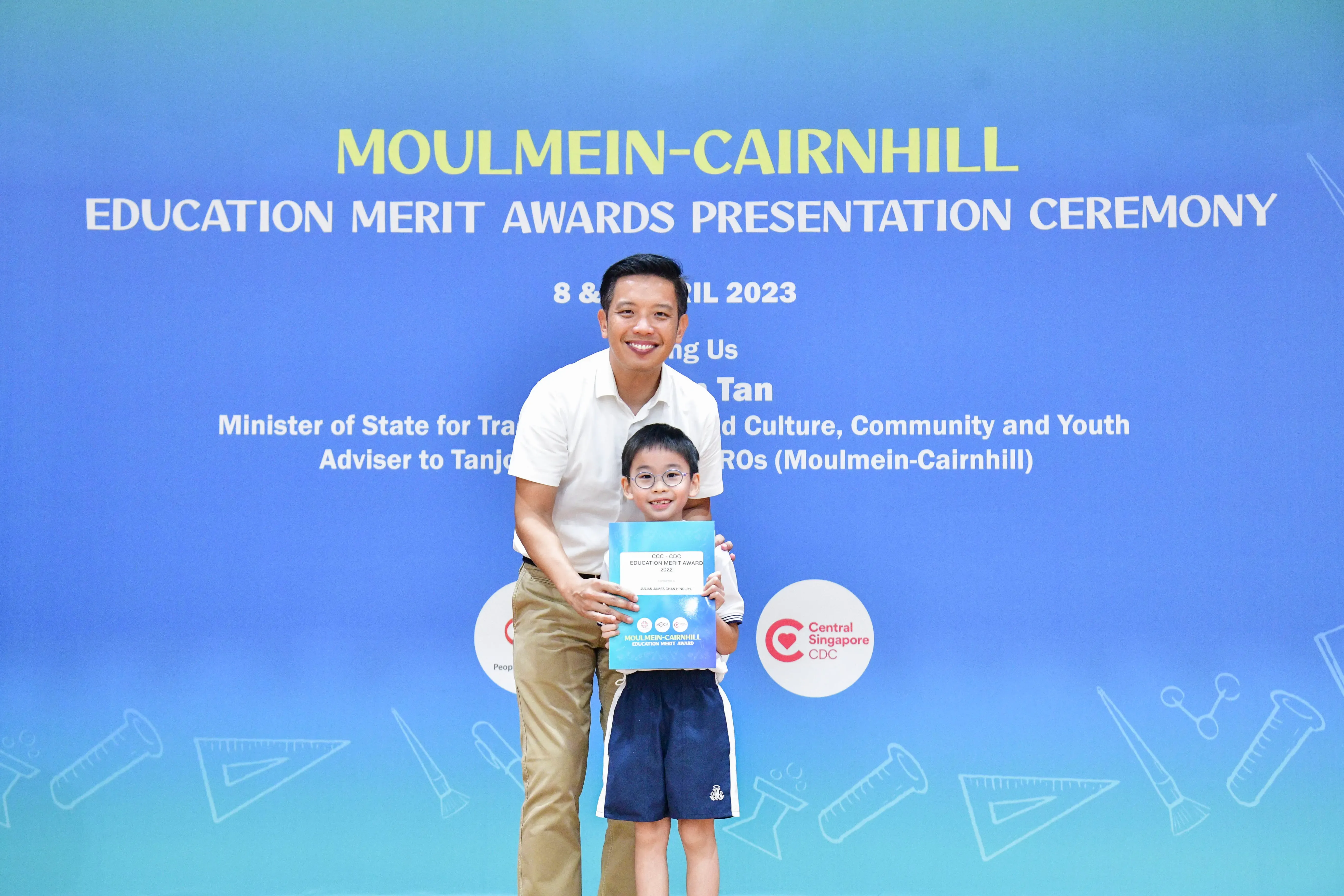 A man and a young boy holding an award certificate at the Moulmein-Cairnhill Education Merit Awards Ceremony 2023.