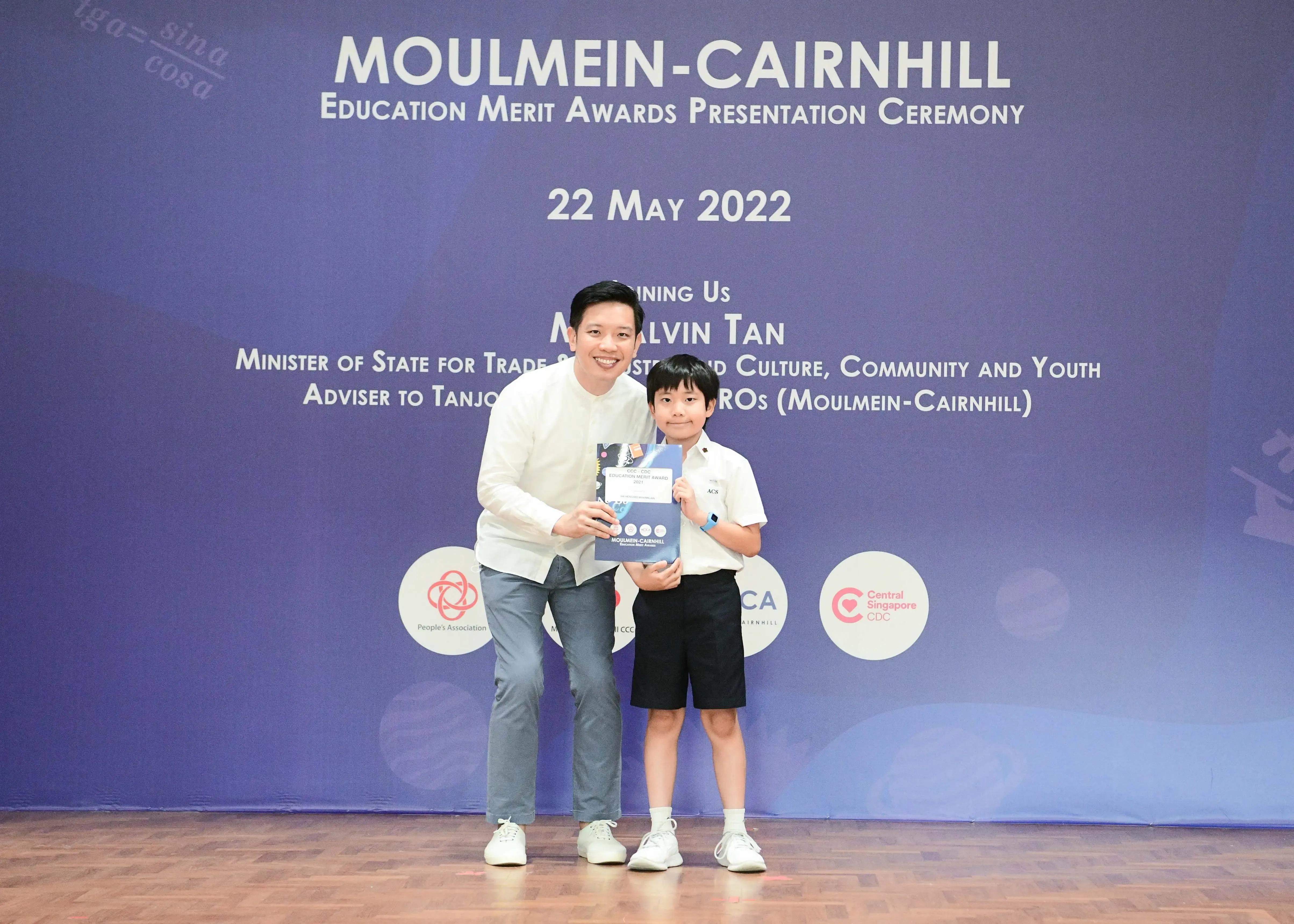 An adult and a young boy hold an award certificate at the Moulmein-Cairnhill Education Merit Awards on 22 May 2022.