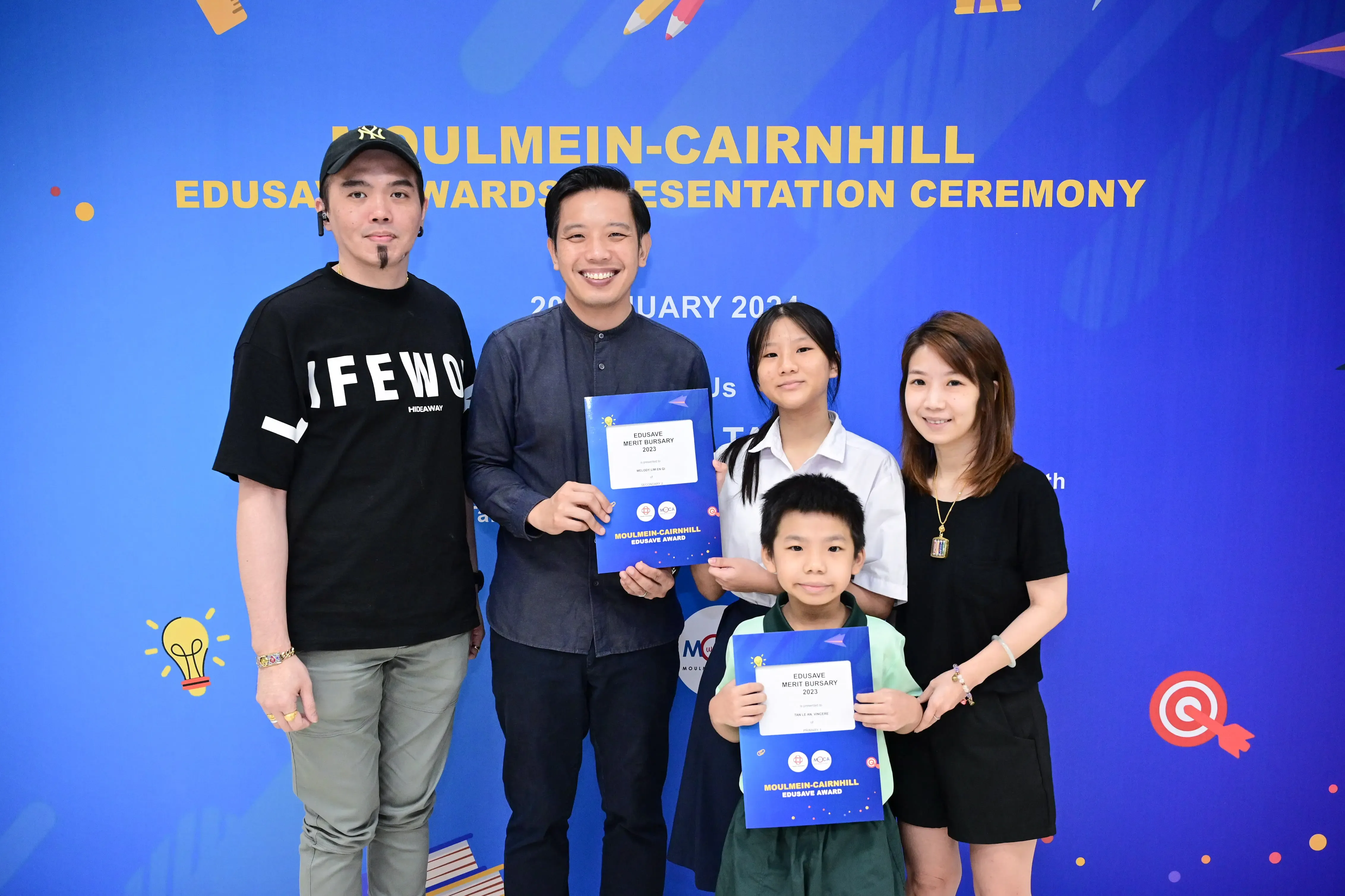 Five people pose at the Moulmein-Cairnhill Edusave Awards Presentation Ceremony, two children holding bursary certificates.