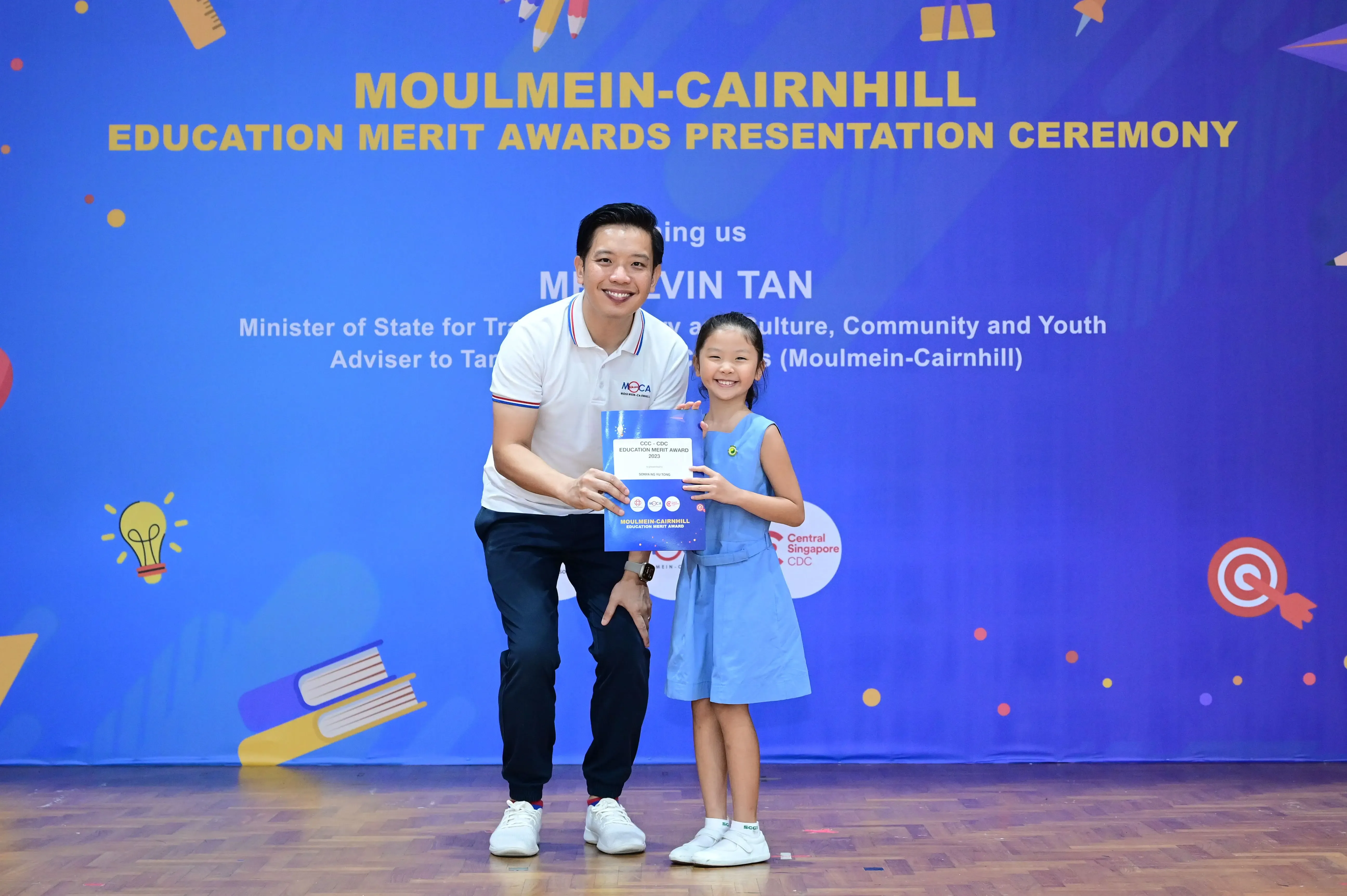 Man and young girl hold an award certificate at Moulmein-Cairnhill Education Merit Awards Presentation Ceremony.