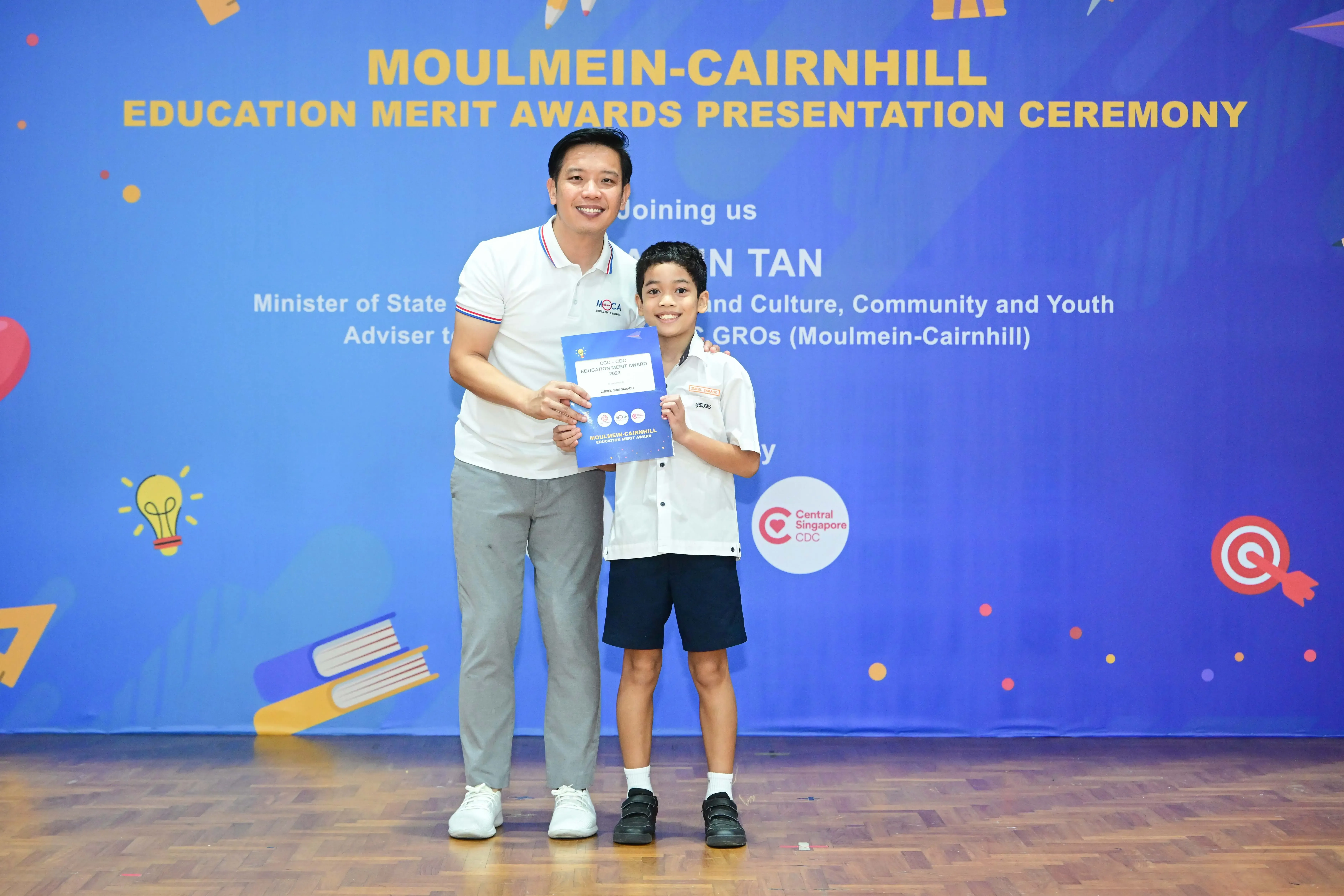 Adult man and young boy holding a certificate at Moulmein-Cairnhill Education Merit Awards Presentation Ceremony.