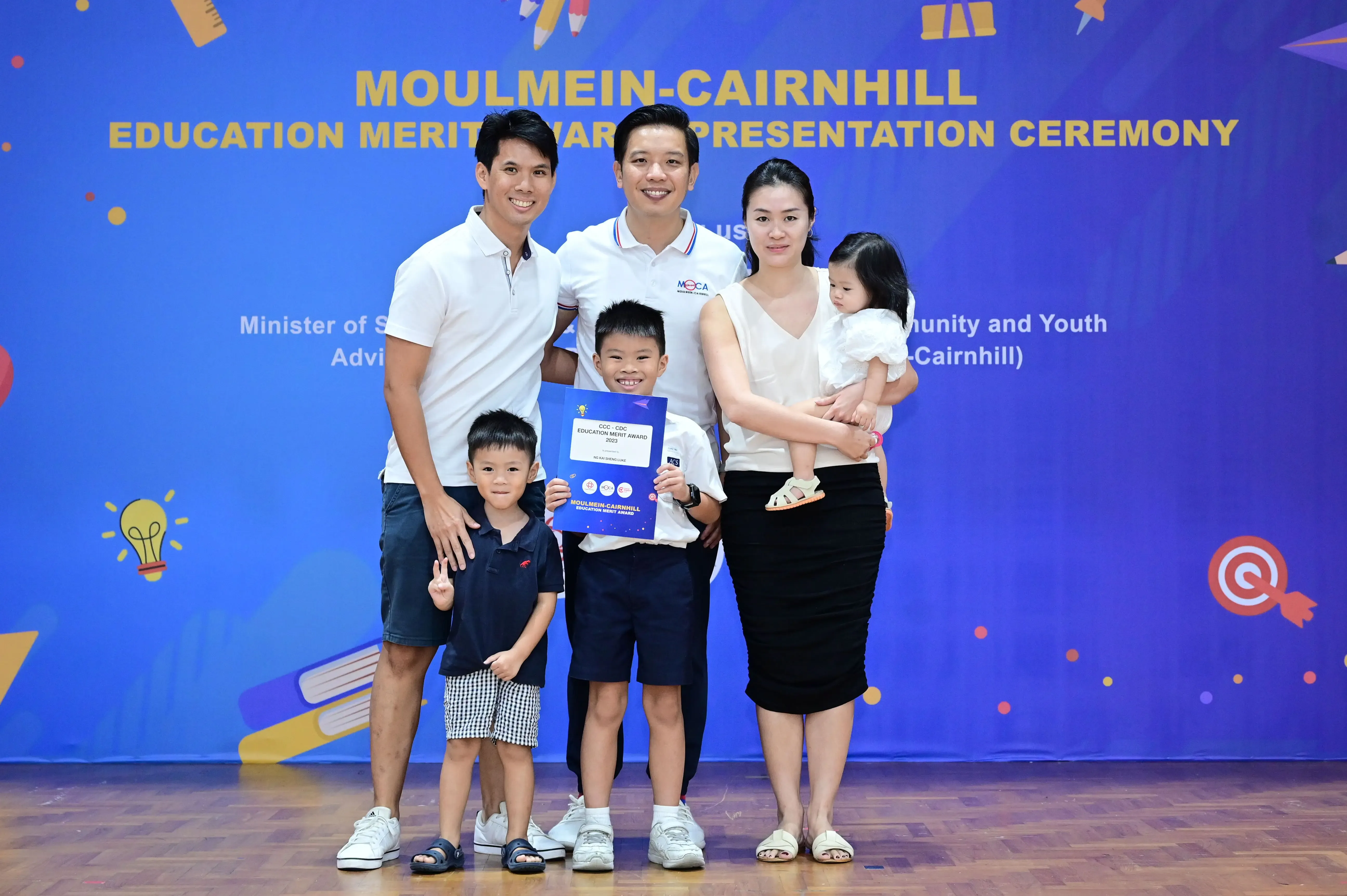 Family of five posing at Moulmein-Cairnhill Education Merit Award ceremony, boy holding a blue certificate.