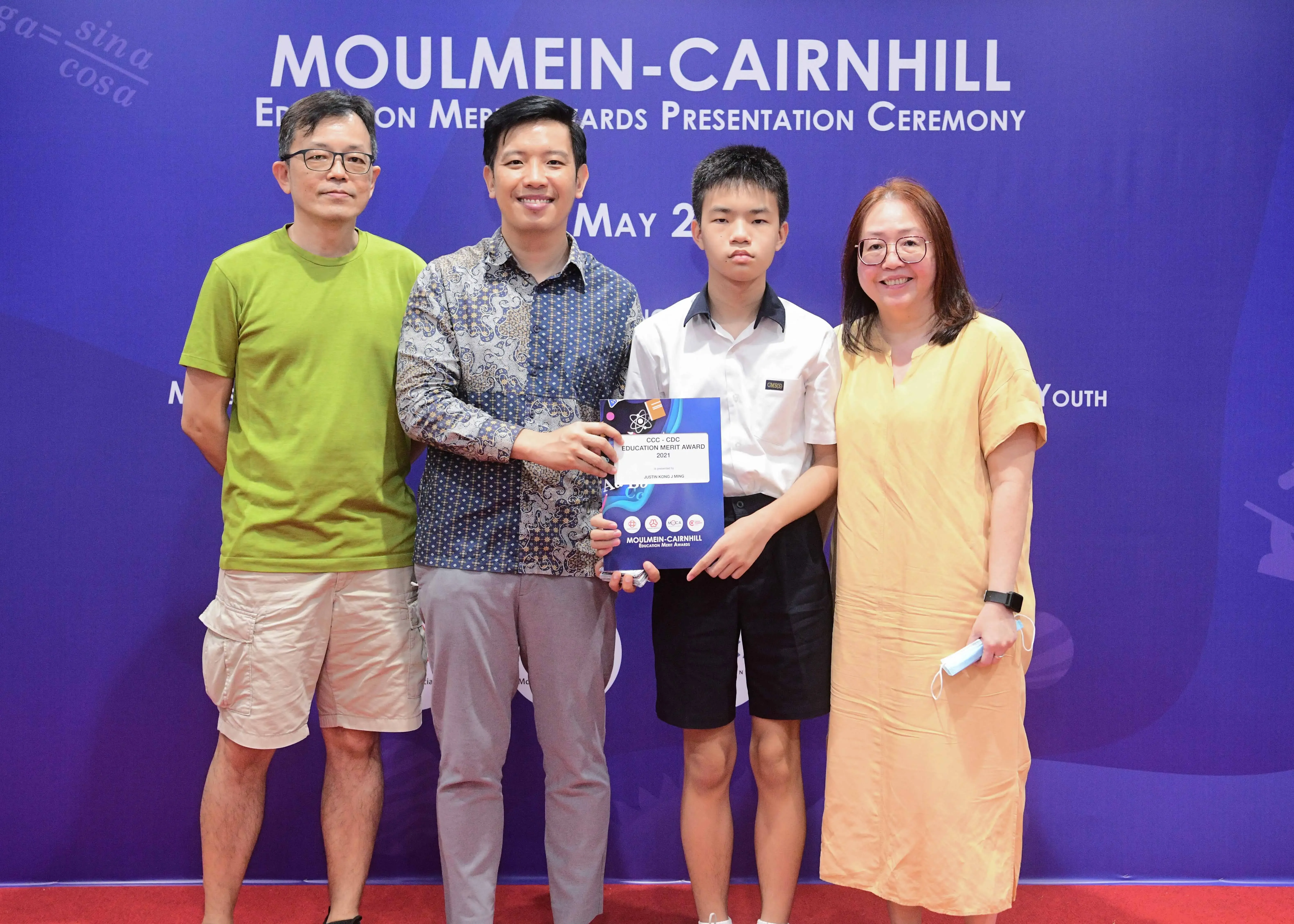 Four people pose at the Moulmein-Cairnhill Education Merit Awards ceremony, with a student holding an award certificate.