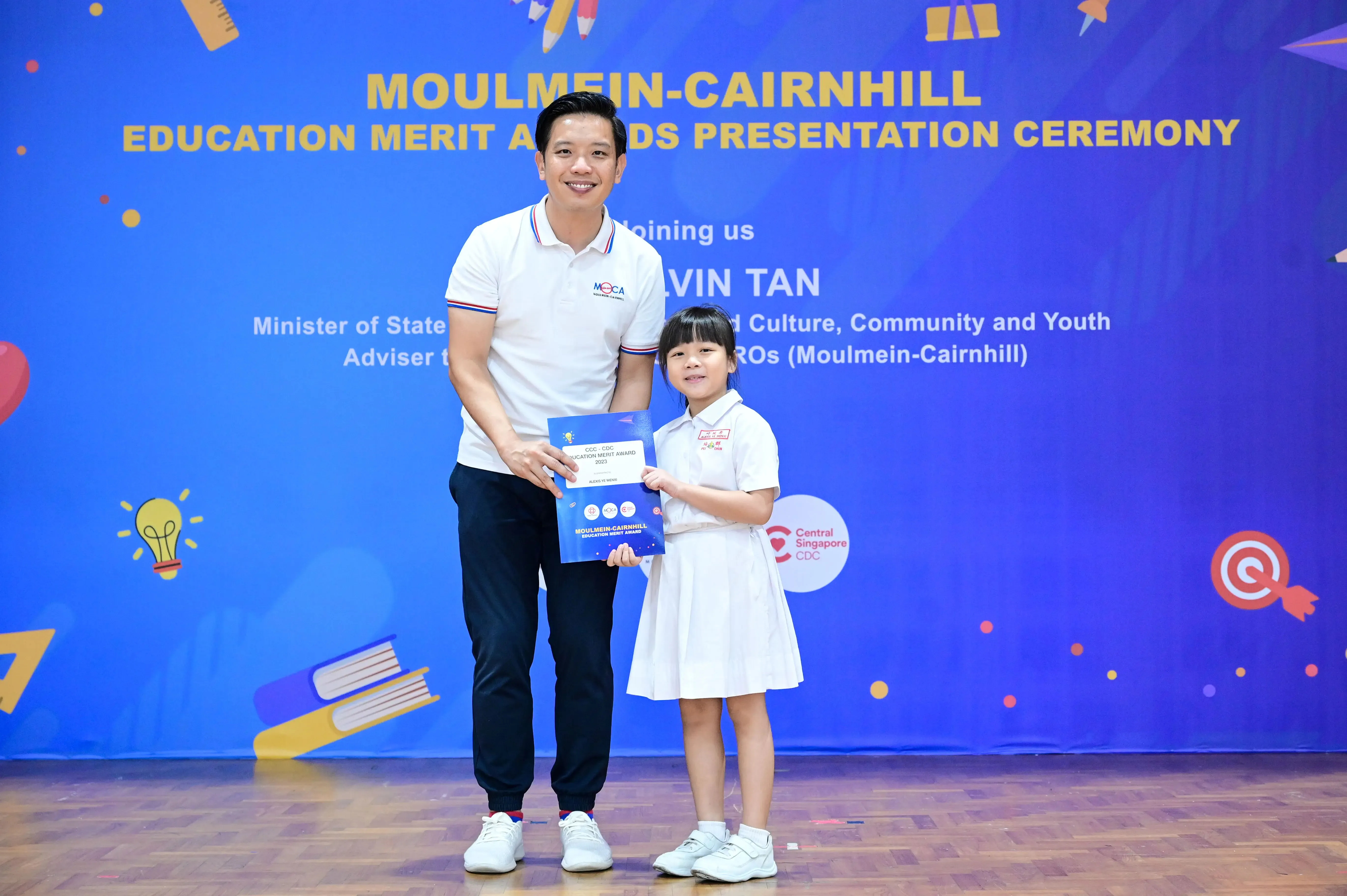 A man and a young girl hold a certificate at the Moulmein-Cairnhill Education Merit Awards Presentation Ceremony.