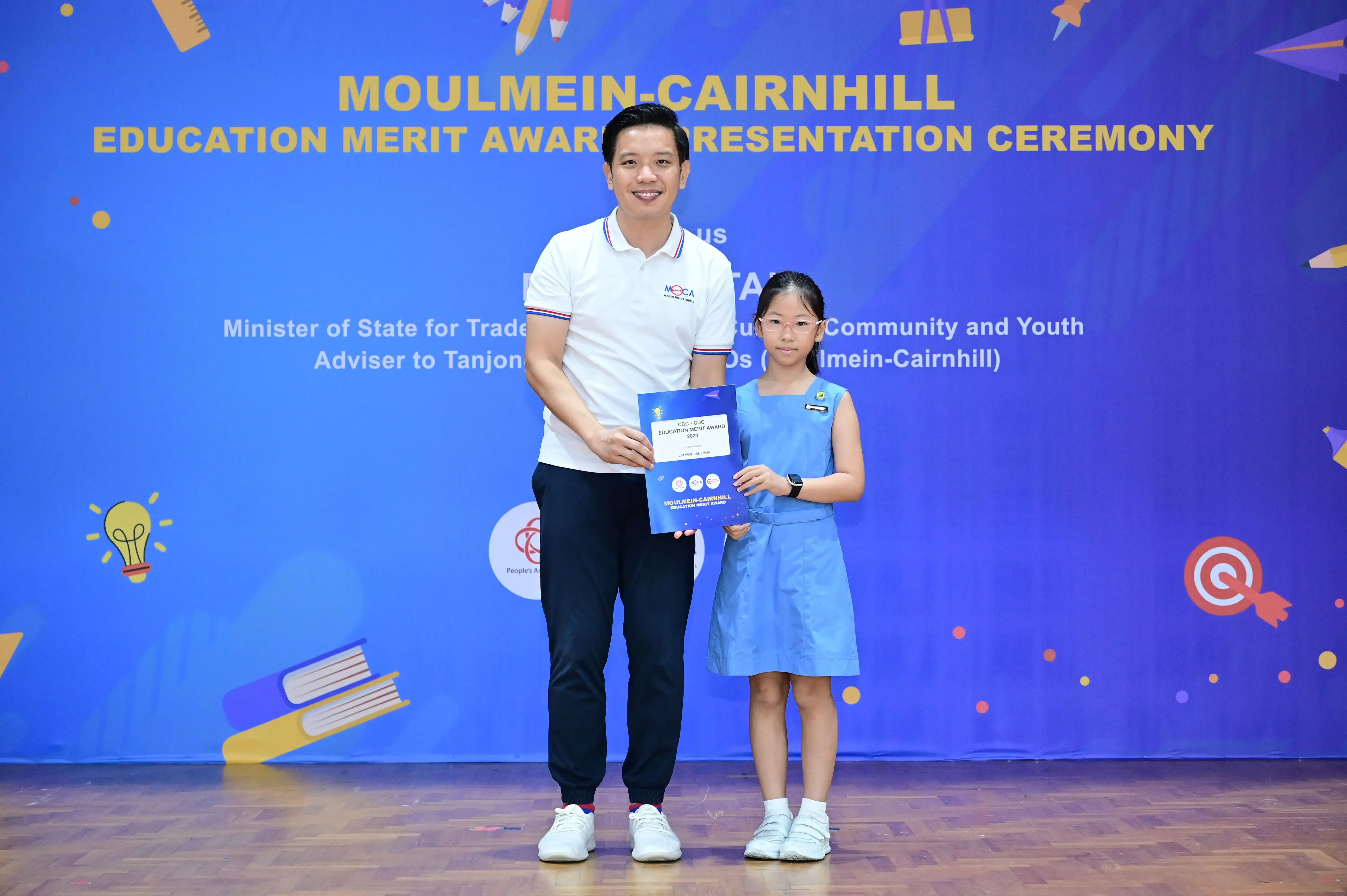 A man and a young girl hold a certificate at the Moulmein-Cairnhill Education Merit Award Presentation Ceremony.