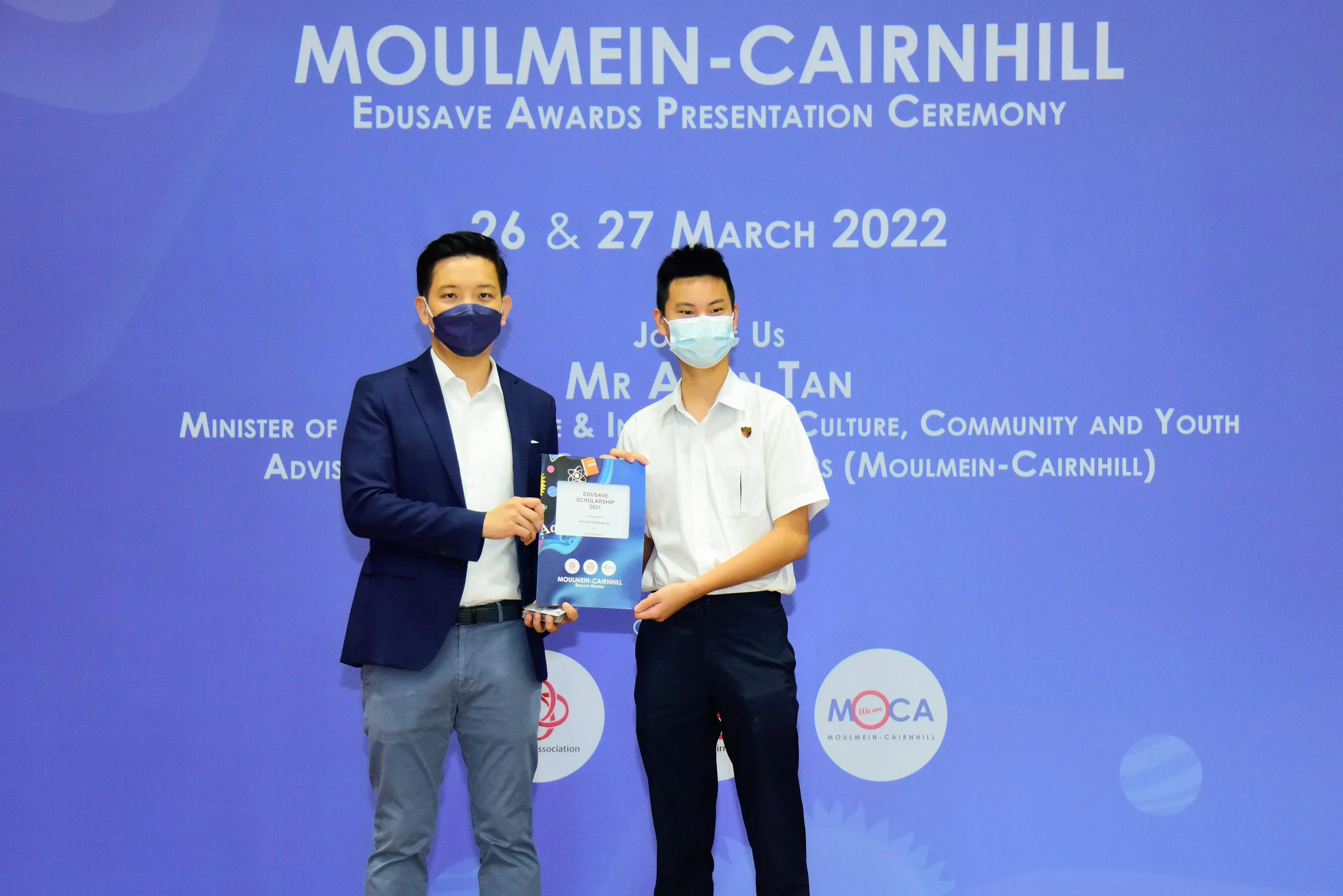 Two masked individuals hold an award certificate at the Moulmein-Cairnhill Edusave Awards Ceremony, March 2022.