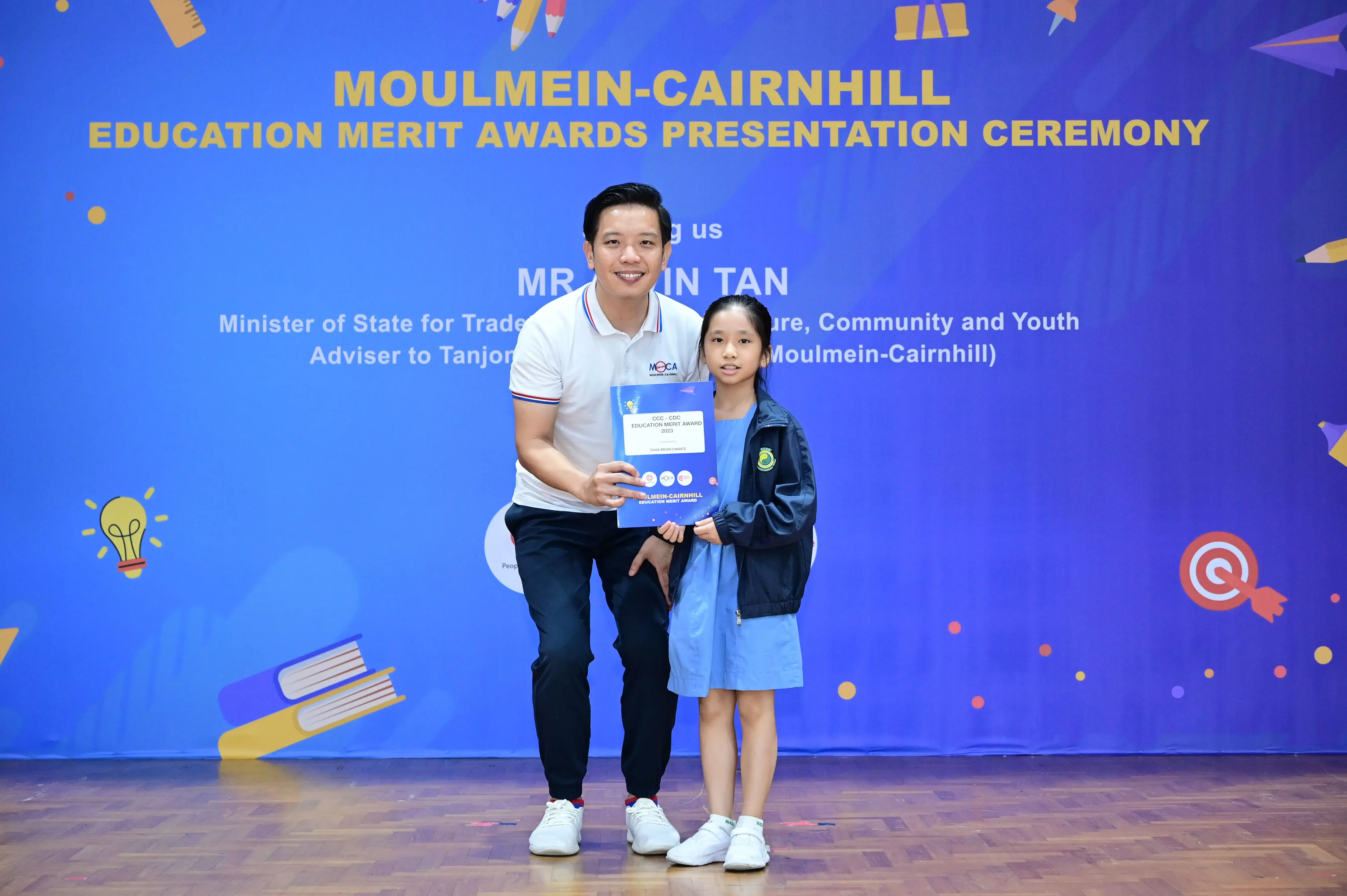 A man and a young girl hold an award certificate at the Moulmein-Cairnhill Education Merit Awards ceremony.