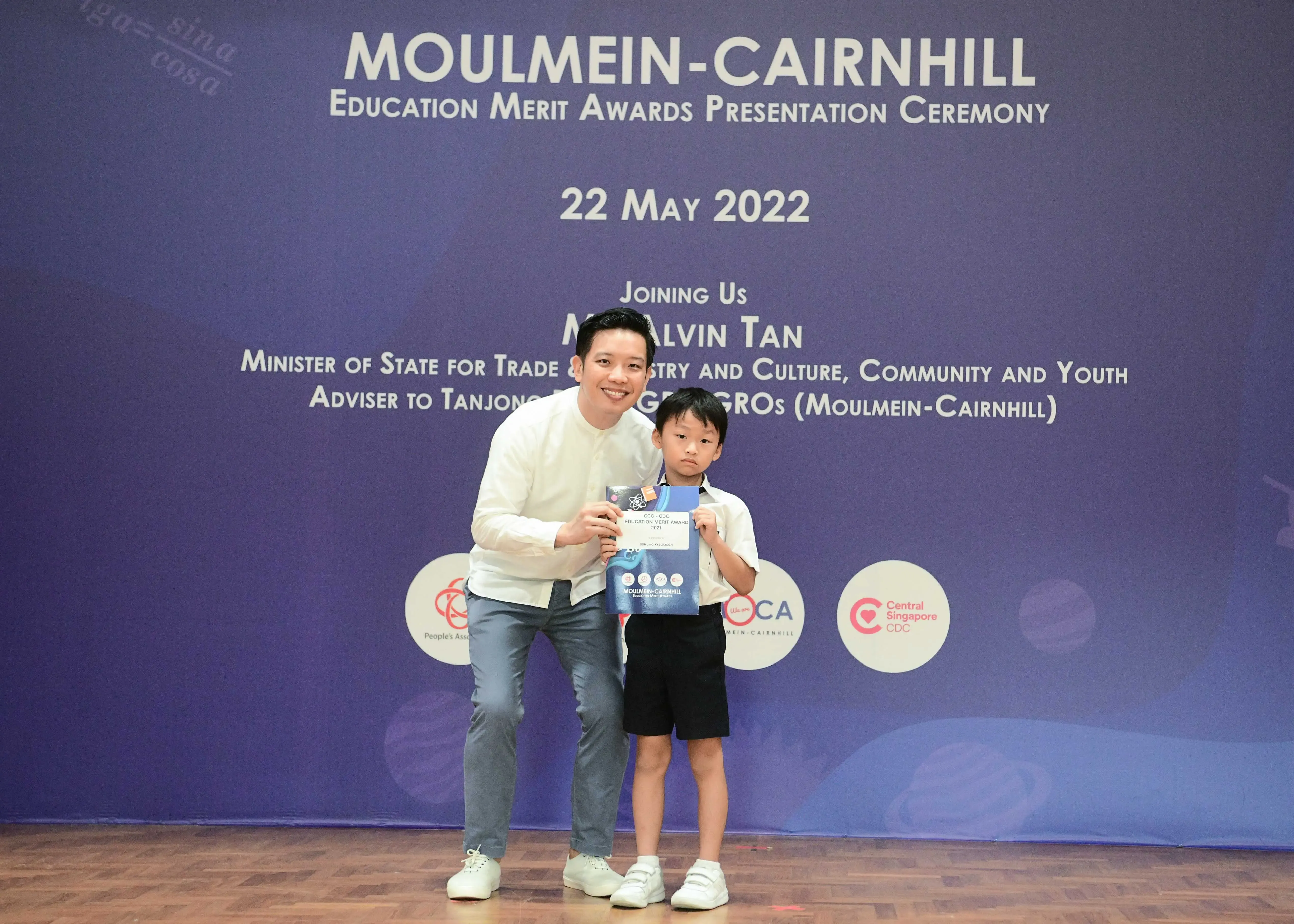 A man and a young boy pose together holding an award certificate at the Moulmein-Cairnhill Education Merit Awards ceremony.