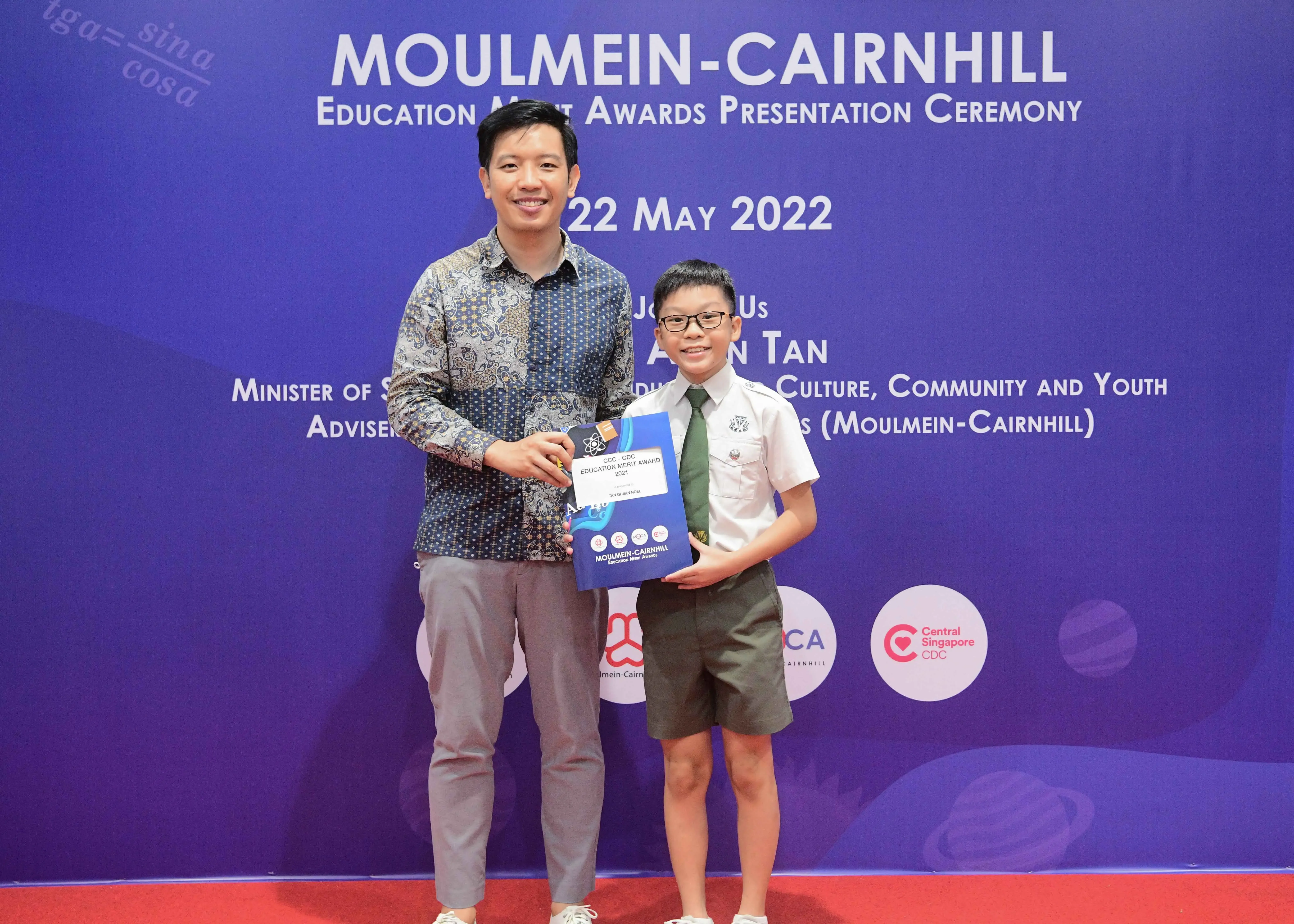 Man and young boy in school uniform hold an award at Moulmein-Cairnhill Education Merit Awards ceremony, 22 May 2022.