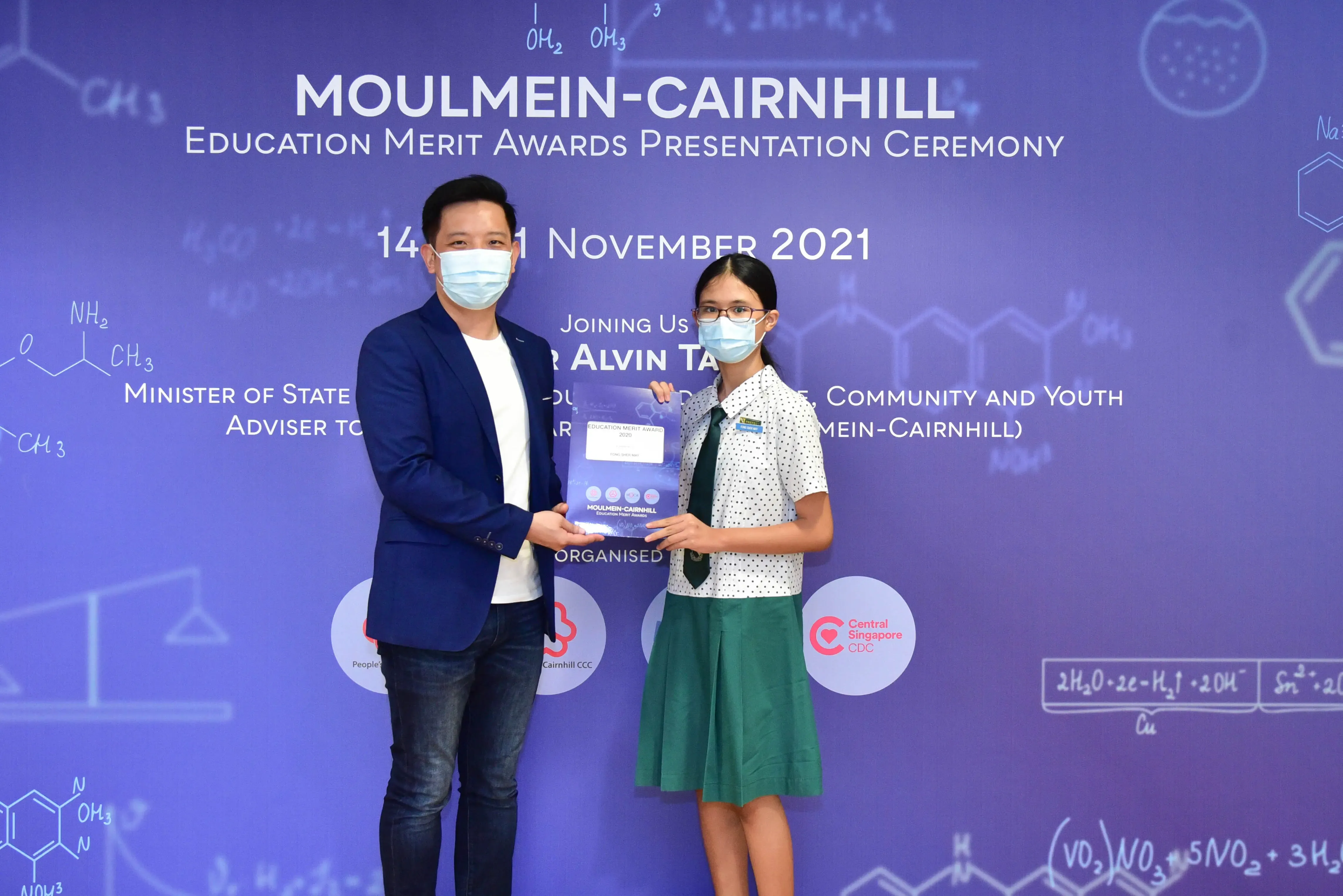 Two masked people hold an award booklet at the Moulmein-Cairnhill Education Merit Awards Ceremony, November 2021.