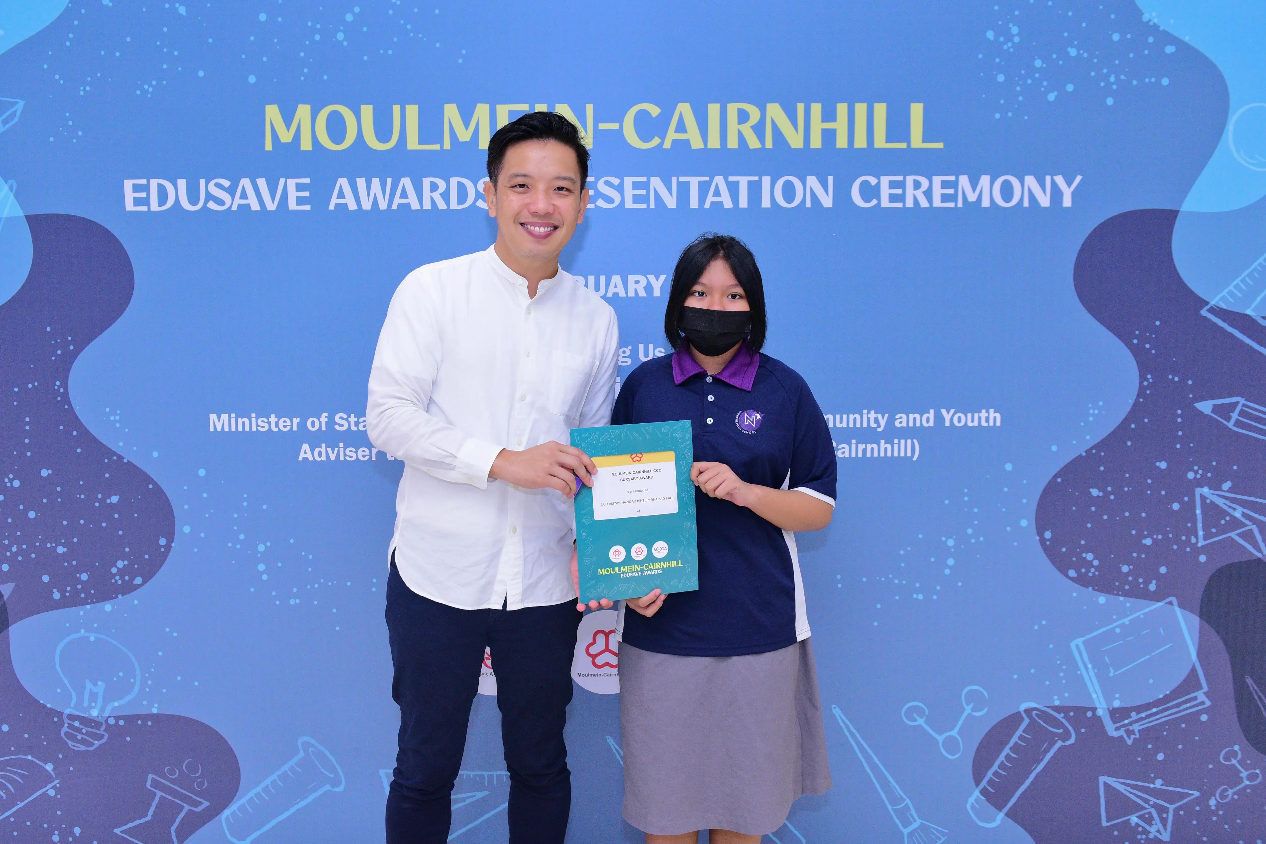 Two people hold a certificate together at the Moulmein-Cairnhill Edusave Awards Presentation Ceremony backdrop.